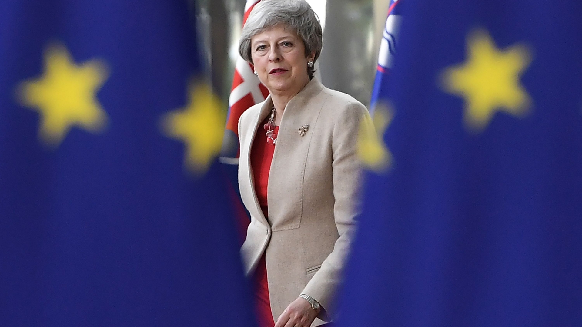 Die britische Premierministerin Theresa May blickt durch zwei EU-Fahnen hindurch.