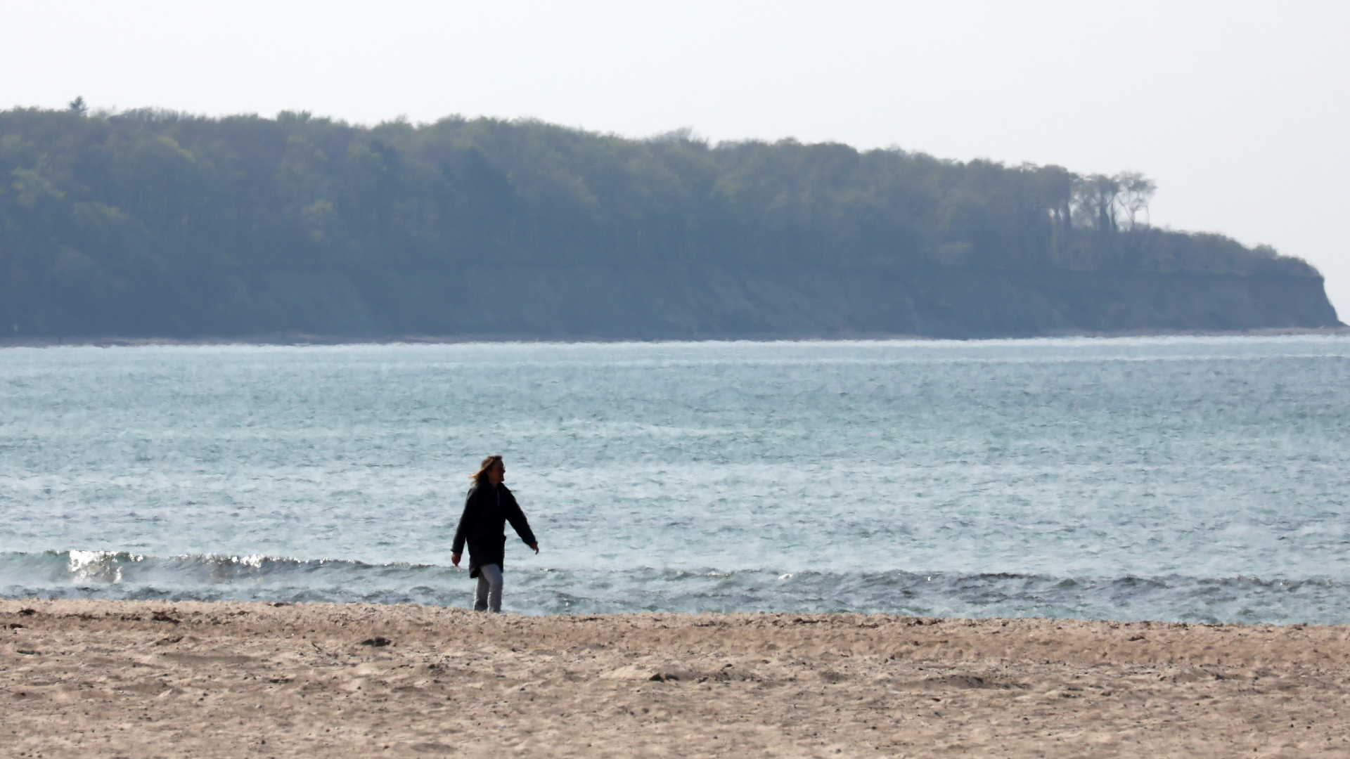 Ein Frau geht am menschenleeren Strand von Warnemünde spazieren. | dpa
