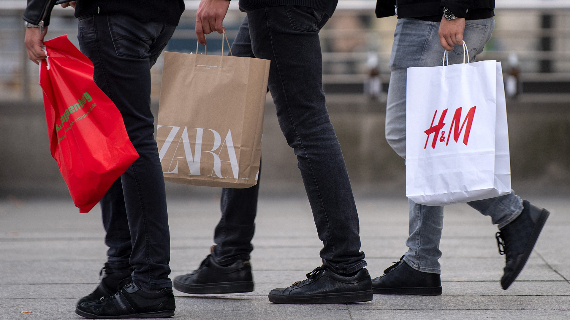 Drei Männer mit Einkaufstüten gehen über eine Straße in der Innenstadt von Berlin | dpa