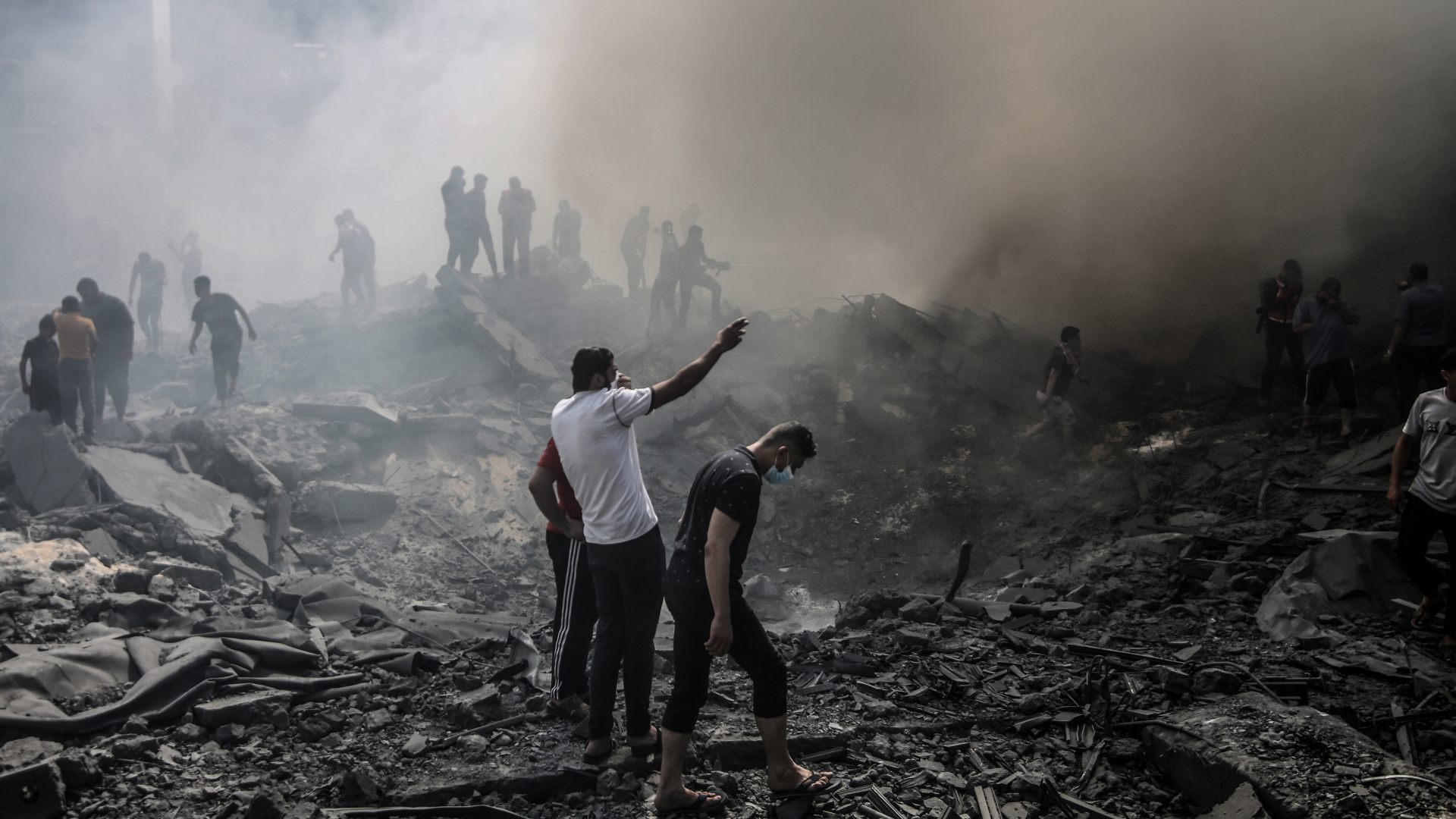 Menschen stehen nach israelischen Luftangriffen zwischen rauchenden Trümmern.