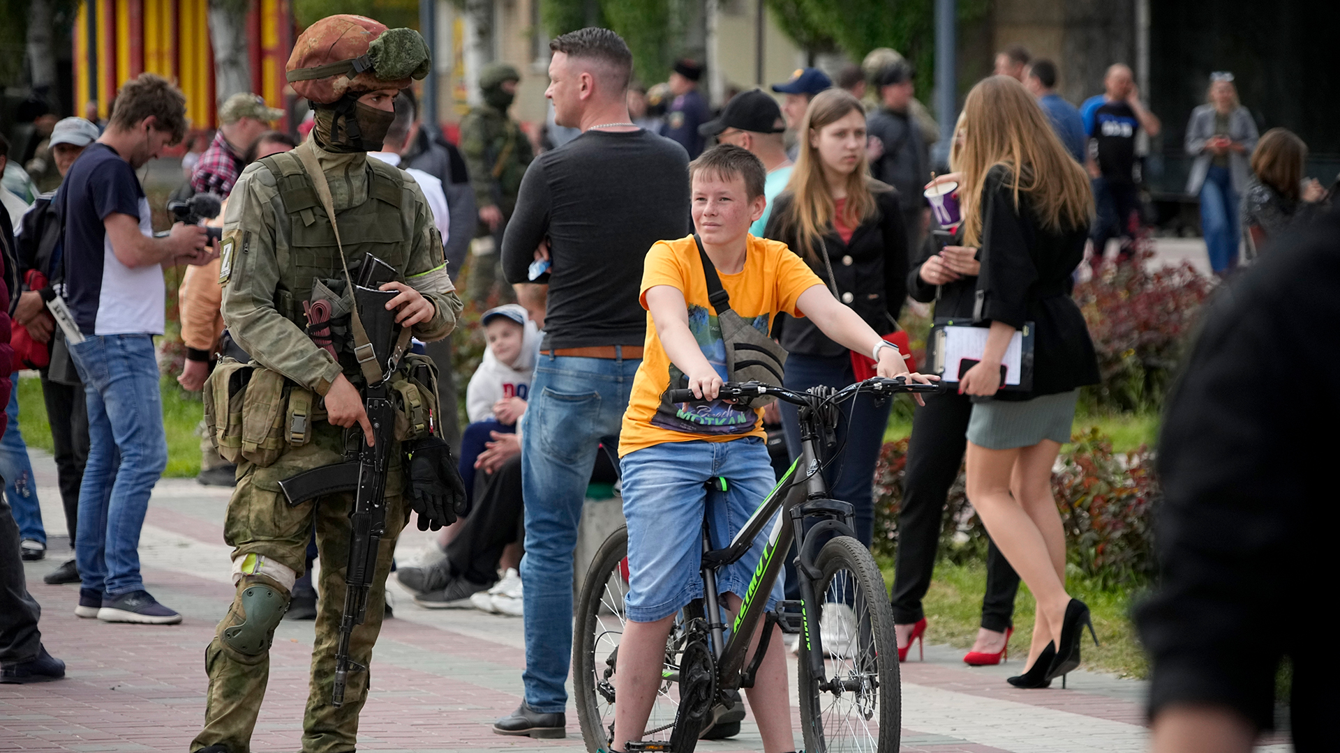 Ein russischer Soldat steht Wache, während Bewohner des Ortes im Zentrum von Melitopol, Region Saporischschja, in einem Gebiet unter russischer Militärkontrolle spazieren gehen.