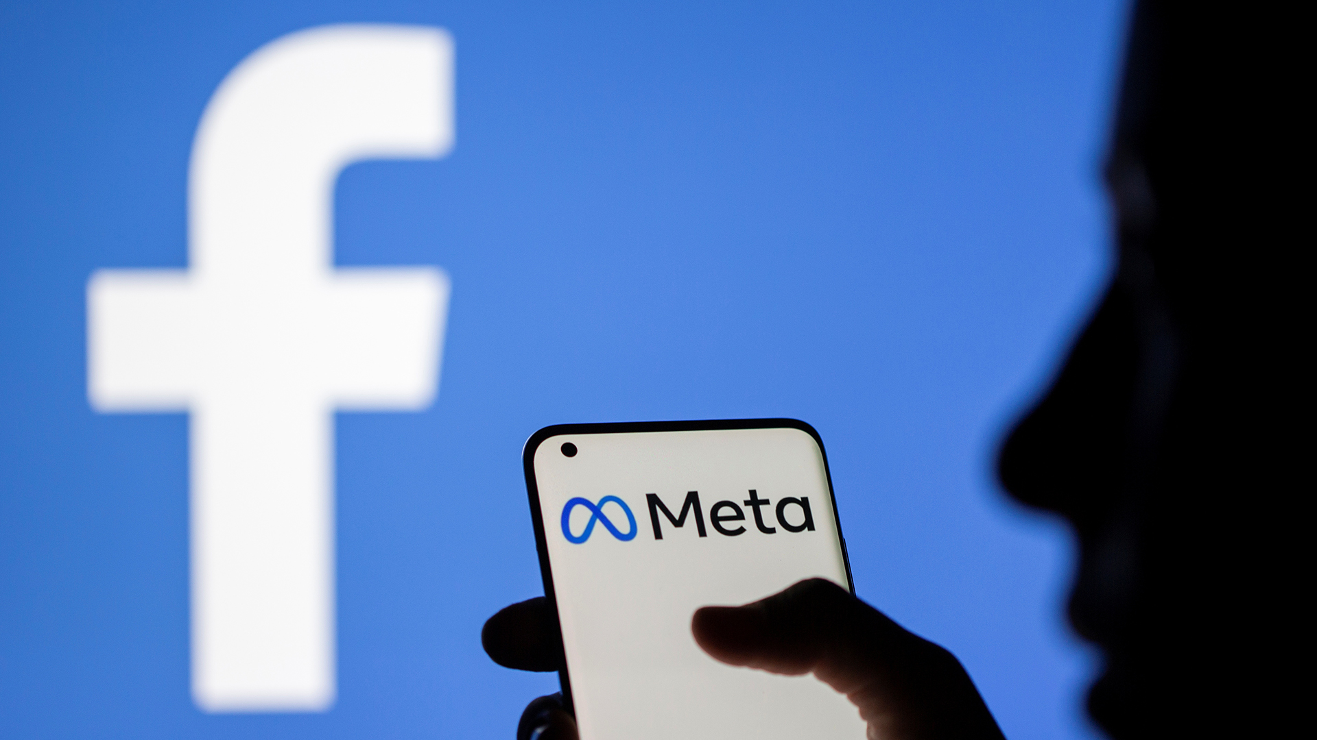 Eine Frau hält ein Smartphone mit einem Meta-Logo vor einem Facebook-Logo. | REUTERS