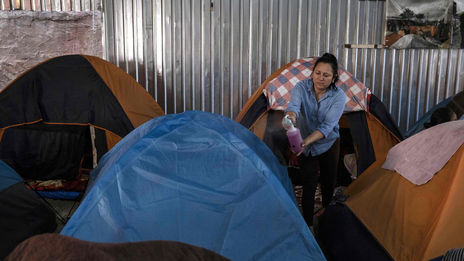 Eine Frau besprüht Zelte, in denen Migrantenin Tijuana untergekommen sind, mit Desinfektionsmittel. | AFP