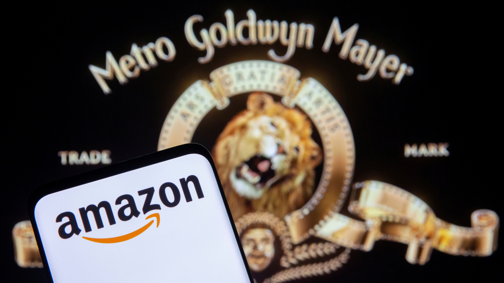 Ein Smartphone mit dem Amazon-Logo vor einem Bildschirm mit dem MGM-Studios-Logo | REUTERS