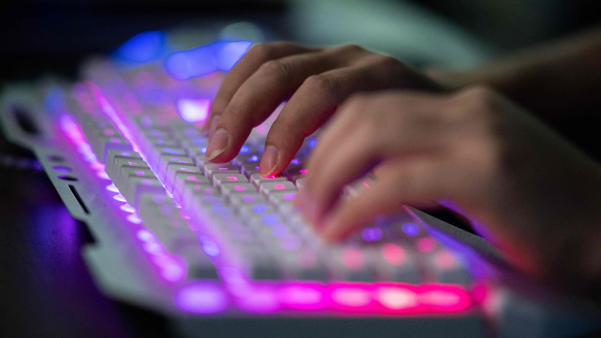 Hände tippen auf einer bunt beleuchteten Tastatur.