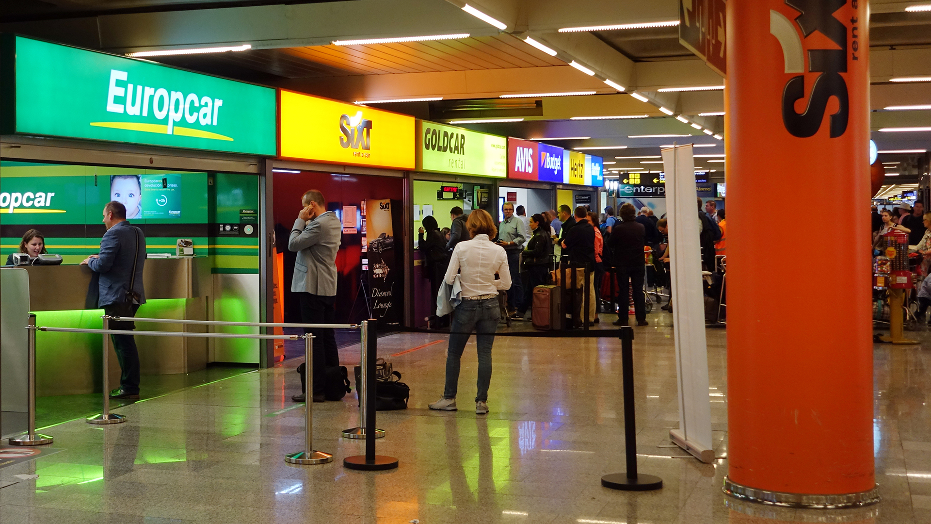 Kunden stehen vor Schalten verschiedener Mietwagenfirmen am Flughafen von Palma de Mallorca