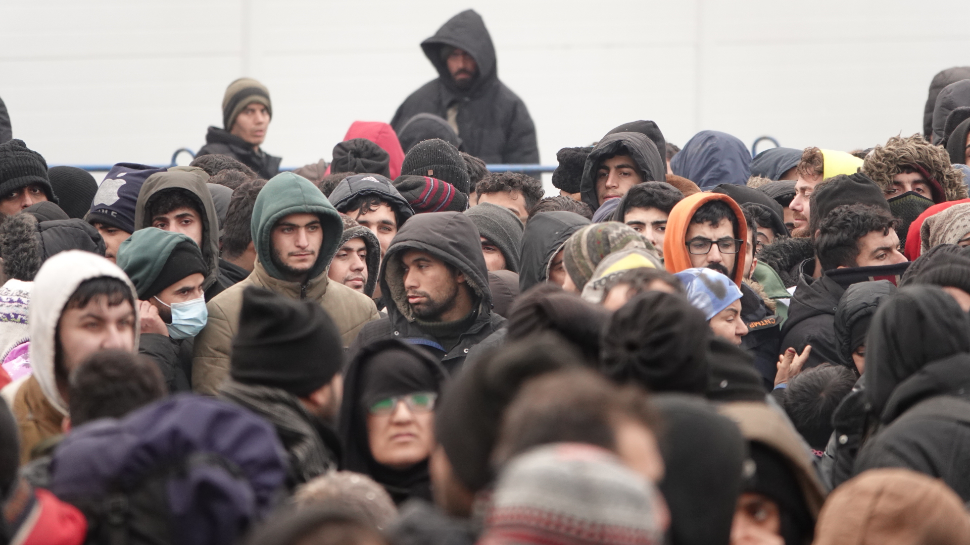 Migranten warten vor einer Lagerhalle in der Nähe der Grenze, die als Notunterkunft eingerichtet wurde (Archivbild). | dpa
