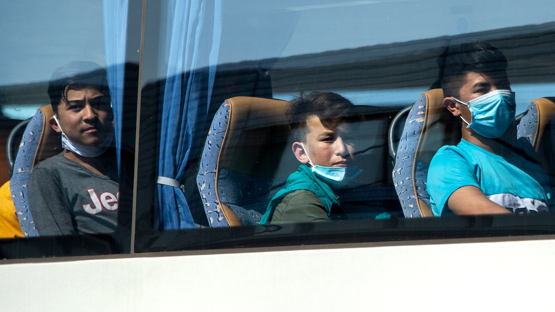Junge Flüchtlinge, teilweise mit Mundschutz, sitzen in einem Bus am Flughafen Hannover, Archivbild | dpa