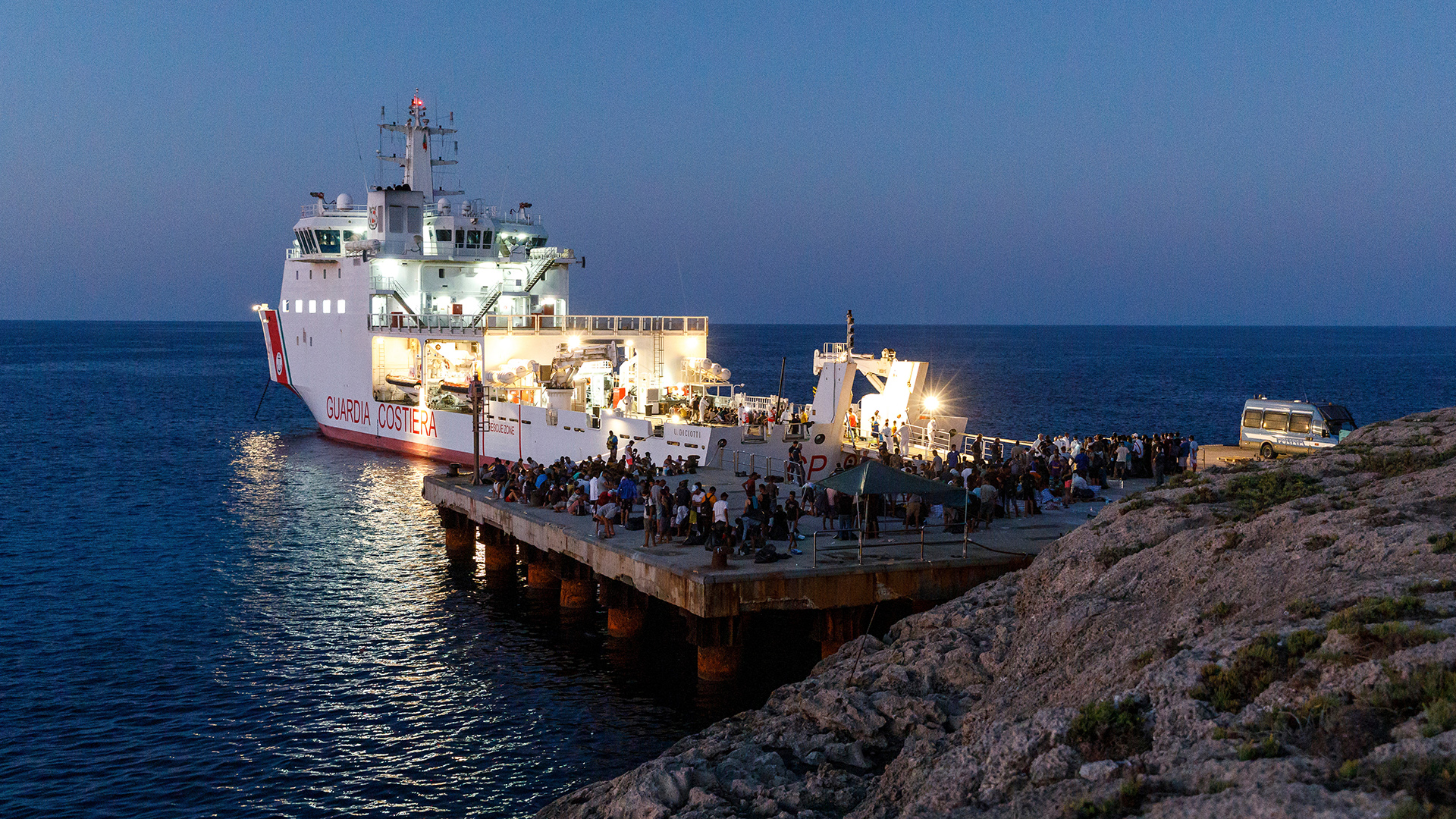 Migranten warten an Bord eines Schiffes der italienischen Küstenwache auf der sizilianischen Insel Lampedusa. | dpa