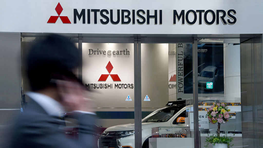 Ein Mann geht an einem Mitsubishi-Logo vorbei