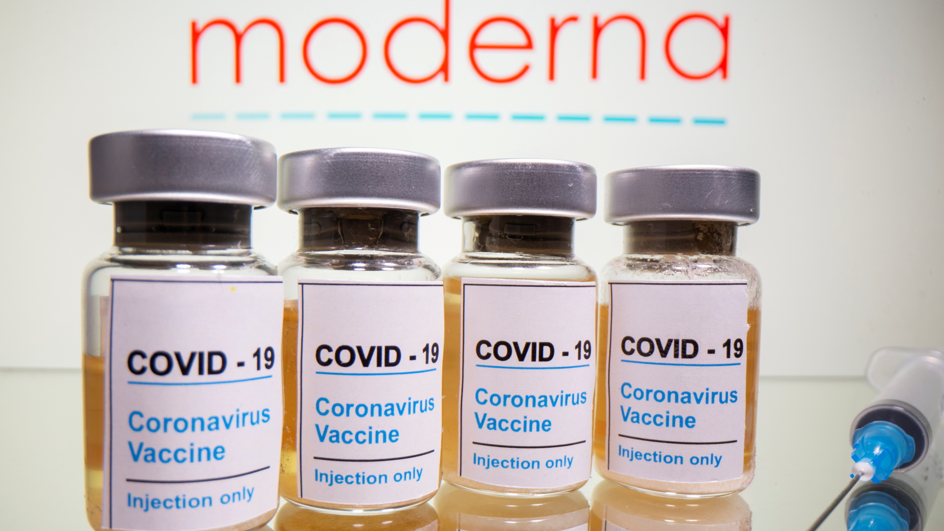 Kleine Behälter mit der Aufschrift "Coronavirus Impfstoff" vor einem Logo des US-Unternehmens Moderna