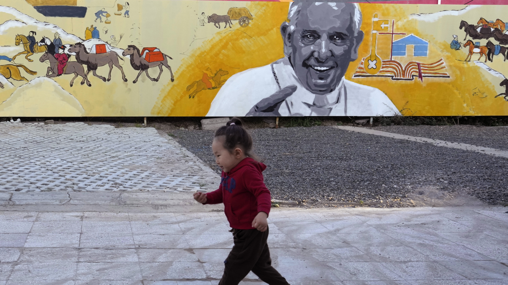 Ein Kind läuft an einem Wandgemälde vorbei, das Papst Franziskus mit einer Darstellung des täglichen Lebens der Nomaden in mongolischer Sprache vor einer Kirche in Ulan Bator.