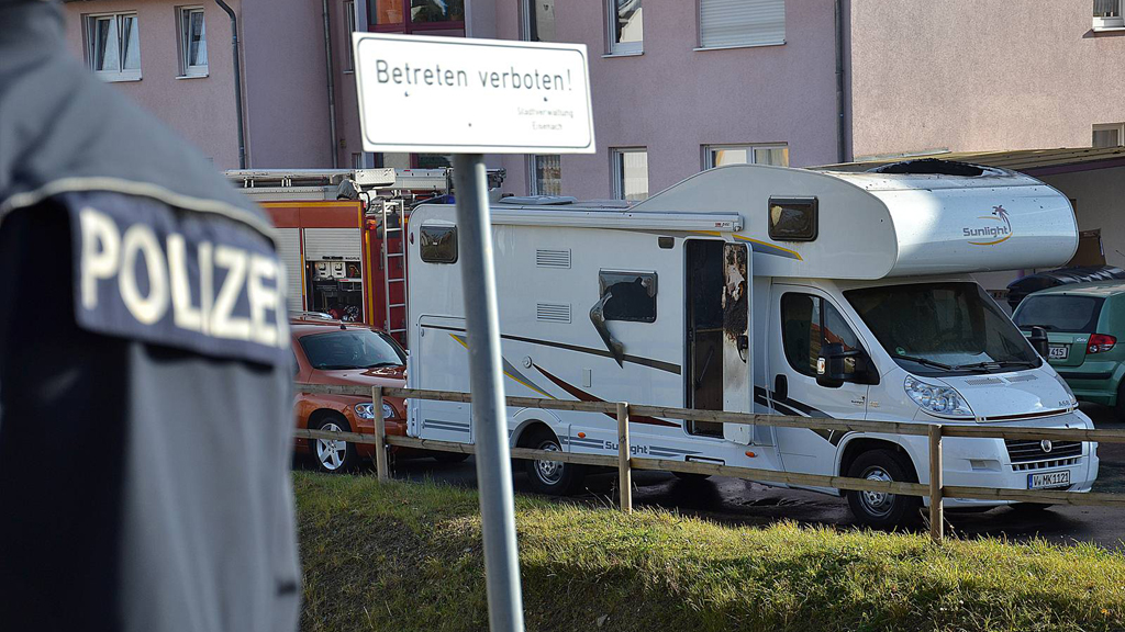 Ein Polizist steht vor einem qualmenden Wohnmobil, in dem die Leichen von Uwe Bönhardt und Uwe Mundlos entdeckt wurden. | picture alliance / dpa