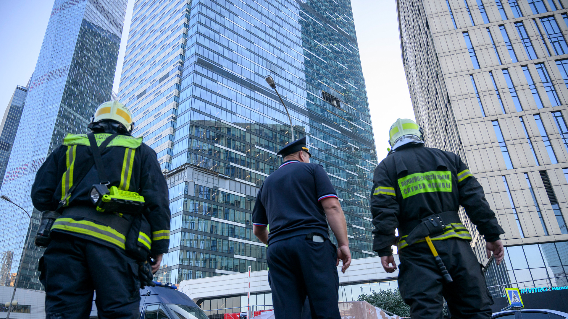 Feuerwehrleute und ein Polizist stehen neben einem beschädigten Gebäude im Geschäftsviertel "Moscow City" nach einem gemeldeten Drohnenangriff in Moskau.