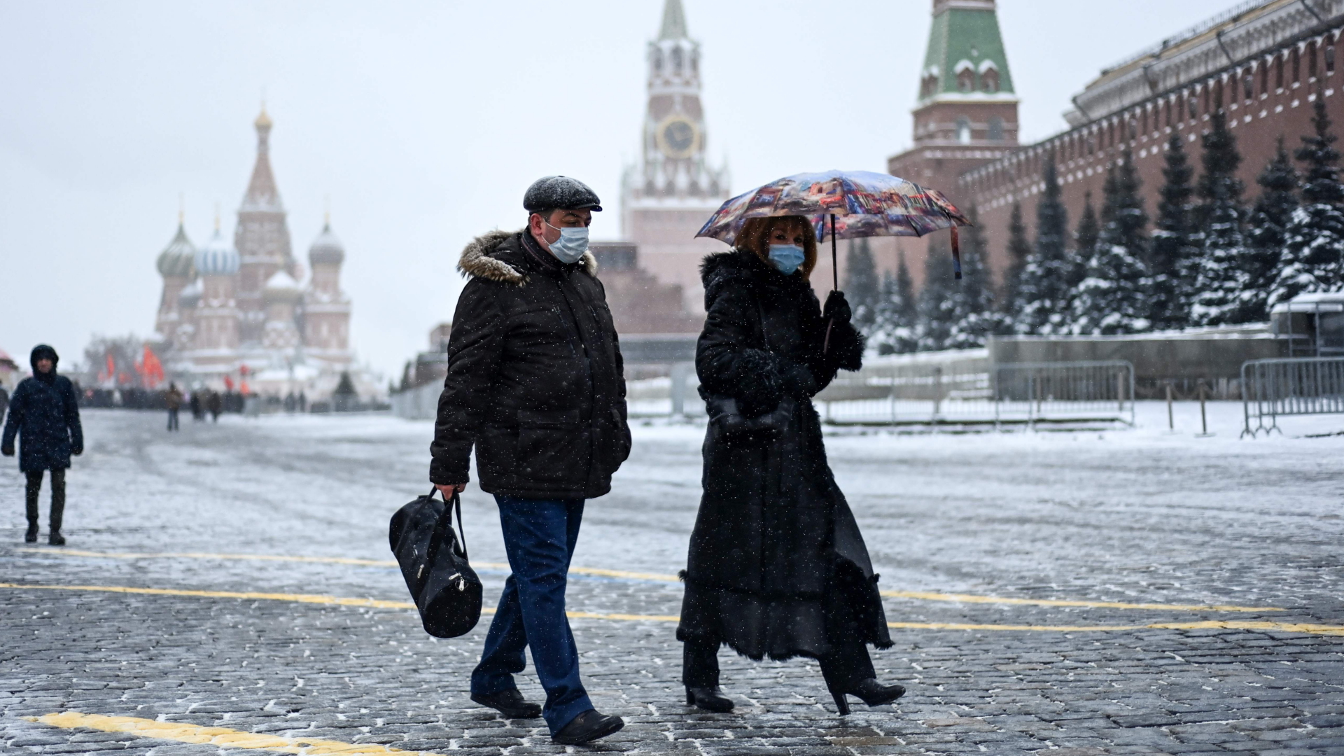 Menschen mit Mund-Nasen-Schutz laufen bei Schneefall über den Roten Platz in Moskau. | AFP