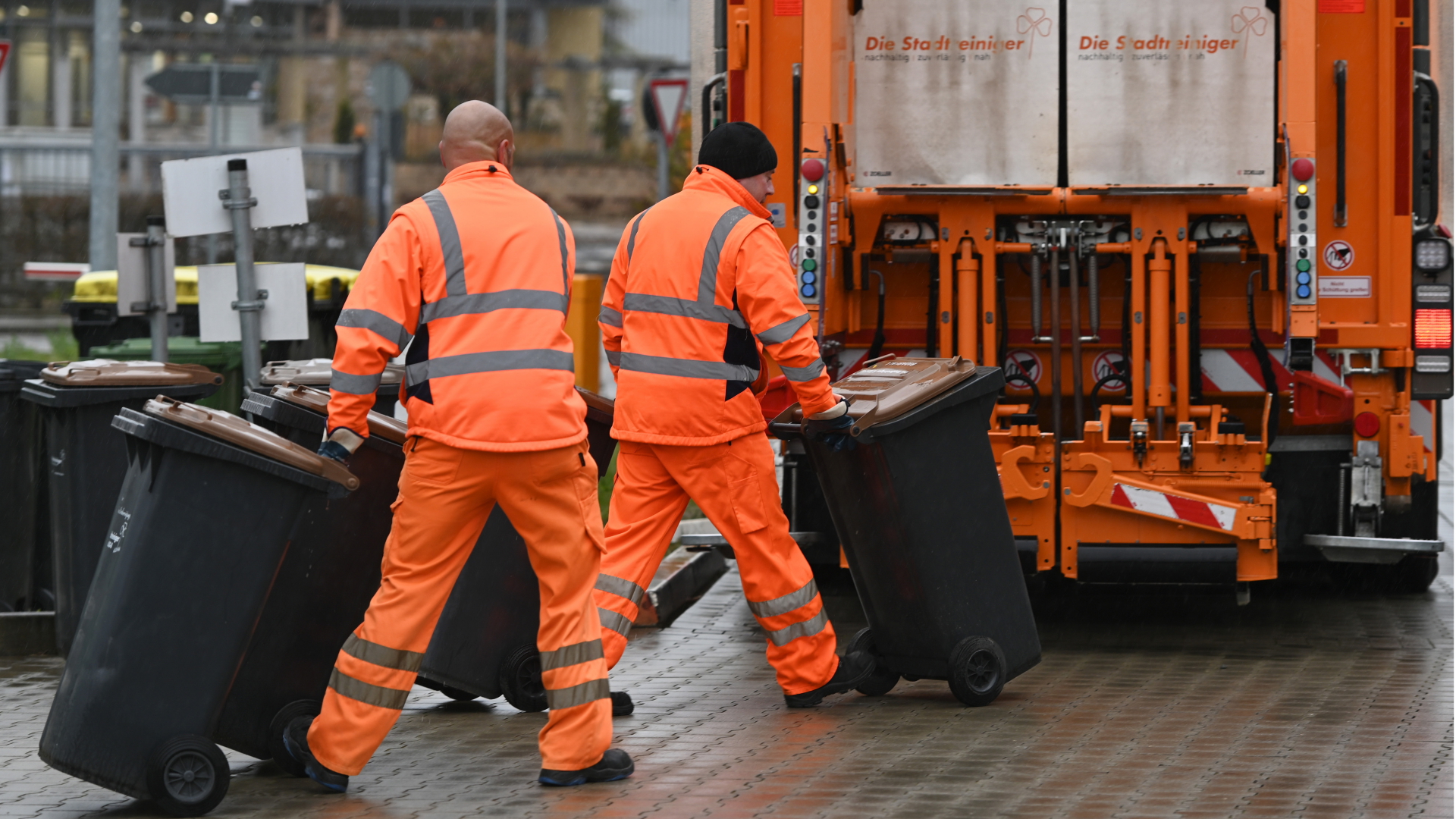 Mitarbeiter der Müllabfuhr rollen Tonnen zum Müllauto