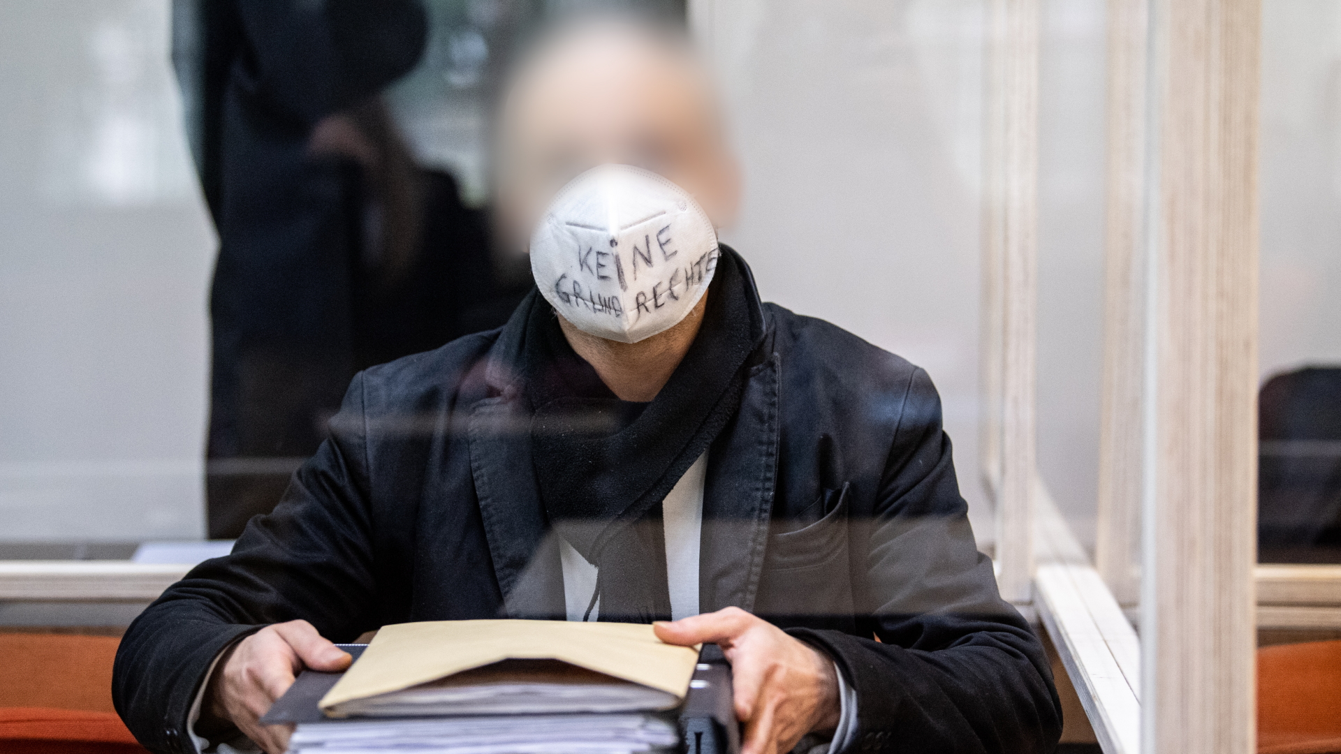 Bayern, München: Ein wegen Subventionsbetrugs angeklagter Mann sitzt zu Prozessbeginn mit einer Maske mit dem Schriftzug ·Keine Grundrechte· in einem Gerichtssaal vom Landgericht München I. | dpa