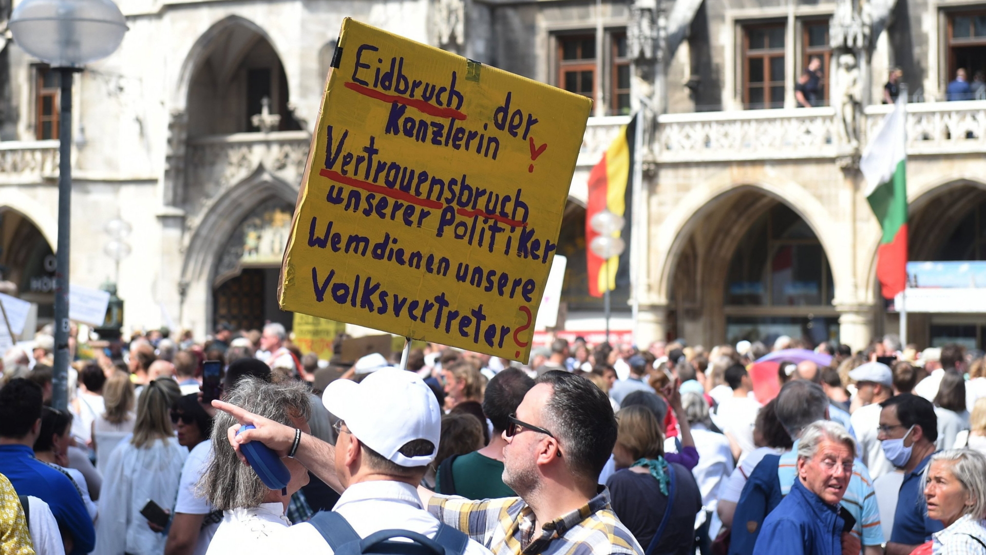 Menschen versammeln sich auf dem Marienplatz um zu demonstrieren, einer der Teilnehmer hält ein Schild mit der Aufschrift "Eidbruch der Kanzlerin". | dpa