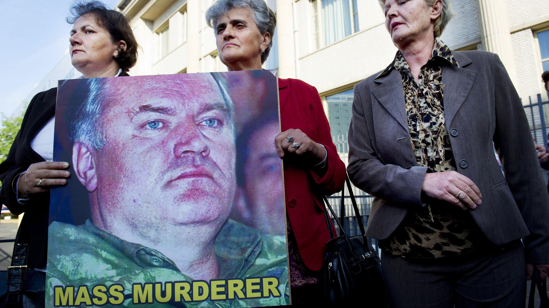 Drei Mütter von Srebrenica mit einem Plakat, das Mladic als Massenmörder verurteilt, vor dem Gericht in Den Haag. | picture alliance / dpa