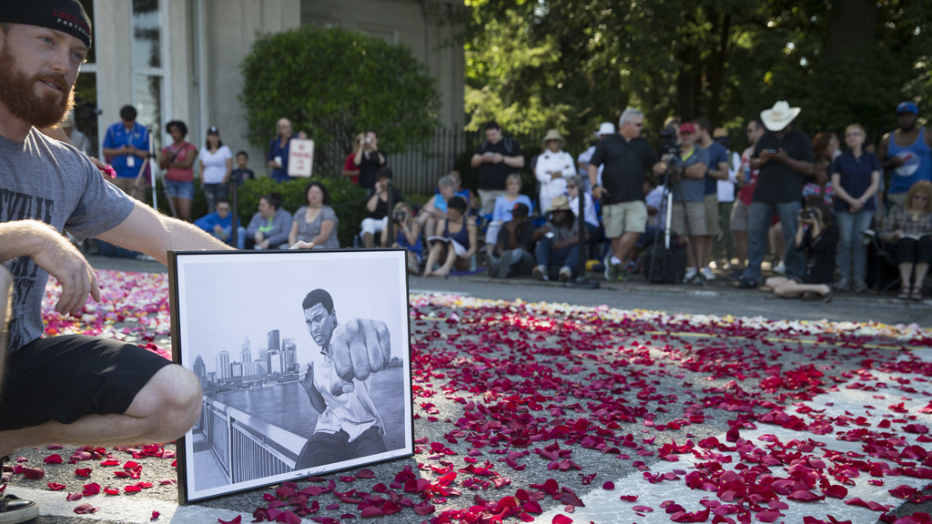 Ein Mann hält ein Porträt von Muhammad Ali auf der mit Rosenblättern übersäten Straße vor dem Friedhof