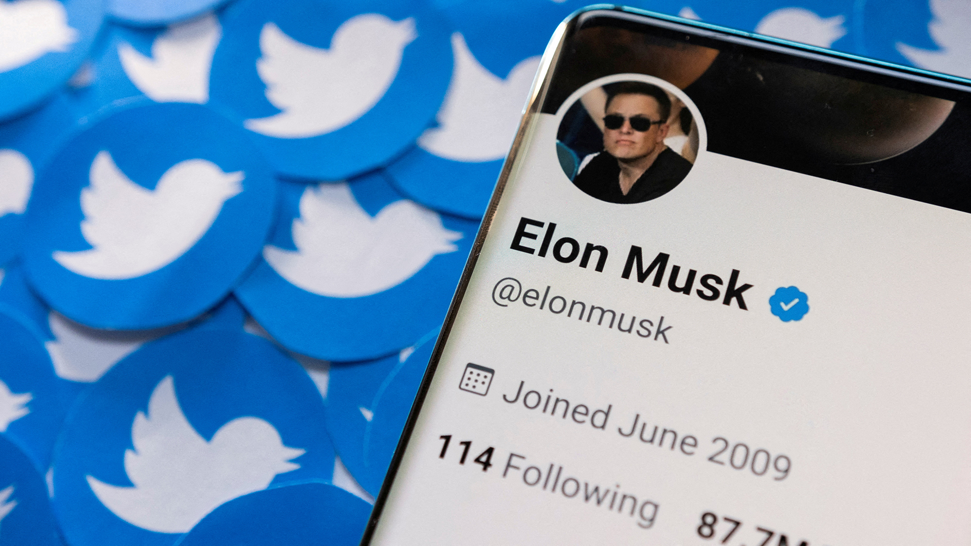 Das Twitter-Profil von Elon Musk ist auf einem Smartphone zu sehen, das auf gedruckten Twitter-Logos platziert ist.