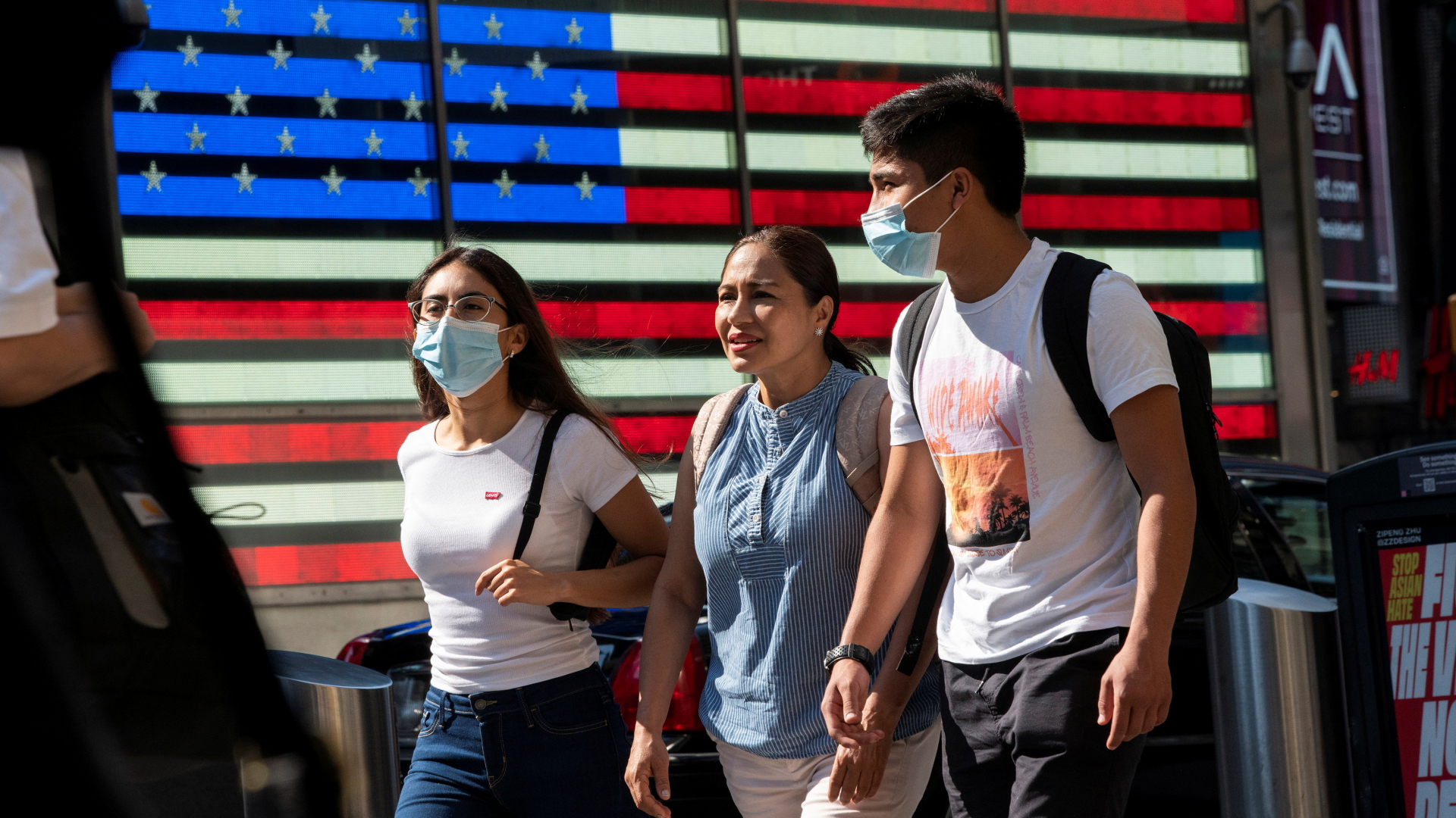 Menschen mit Atemschutzmasken vor einer US-Flagge in New York. | REUTERS