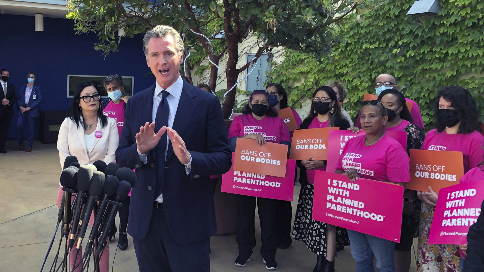 Gavin Newsom hät eine Rede, dahinter stehen mehrere Frauen, sie halten Schilder mit der Aufschrift "I stand with planned parenthood". | AP