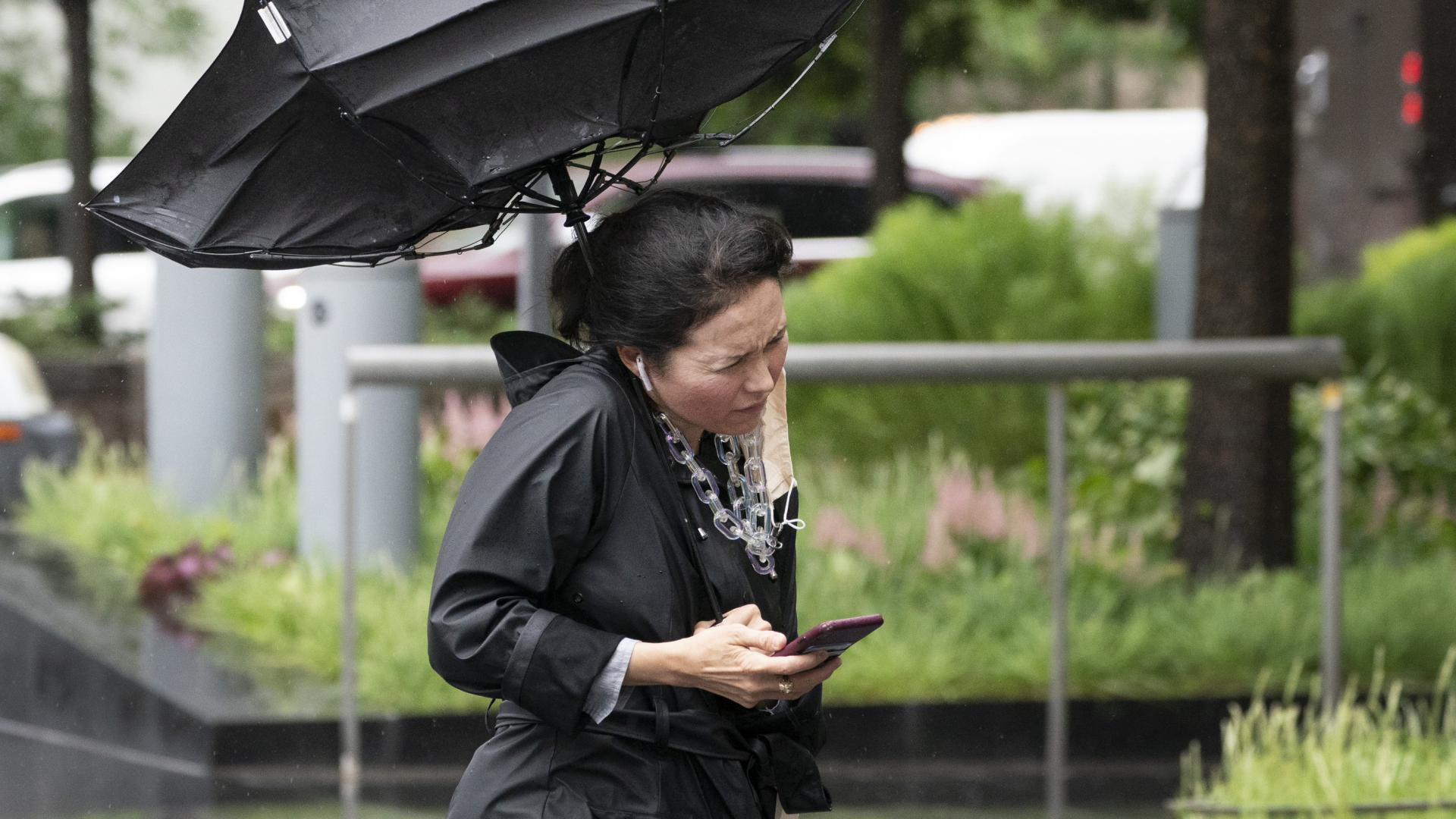 Eine Frau in New York hält bei starkem Regen ein Handy in der Hand. | AP