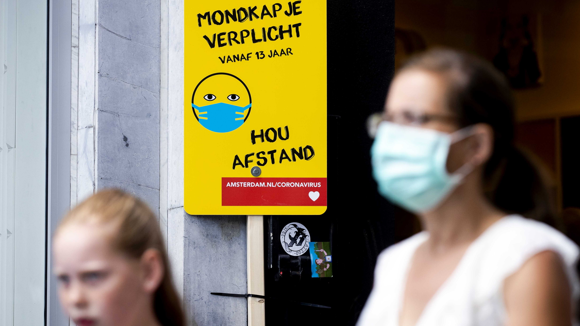 Eine Frau mit Mundschutz geht an einem Schild mit Informationen über die Maskenpflicht vorbei.  | dpa