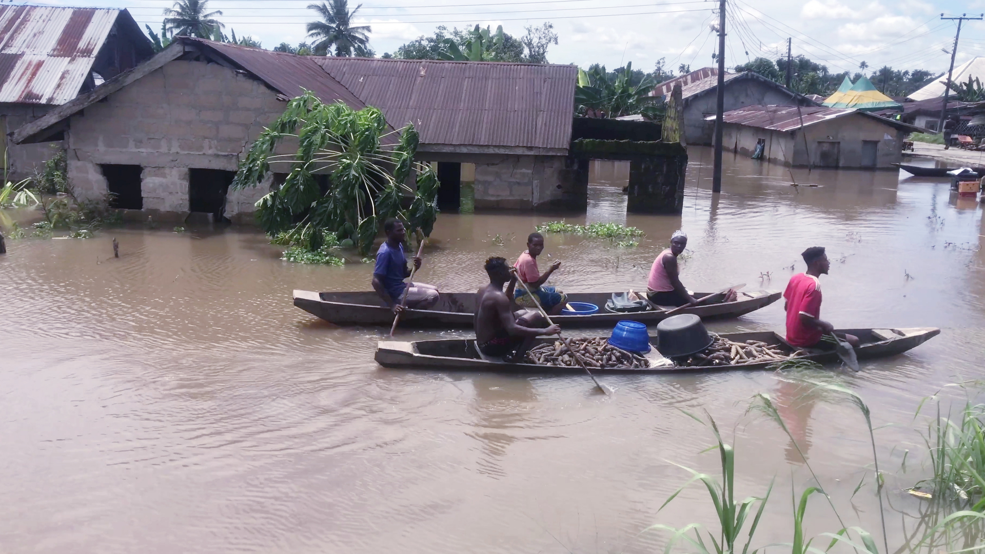 Männer fahren auf zwei Langbooten durch ein überschwemmtes Dorf in Nigeria. | dpa