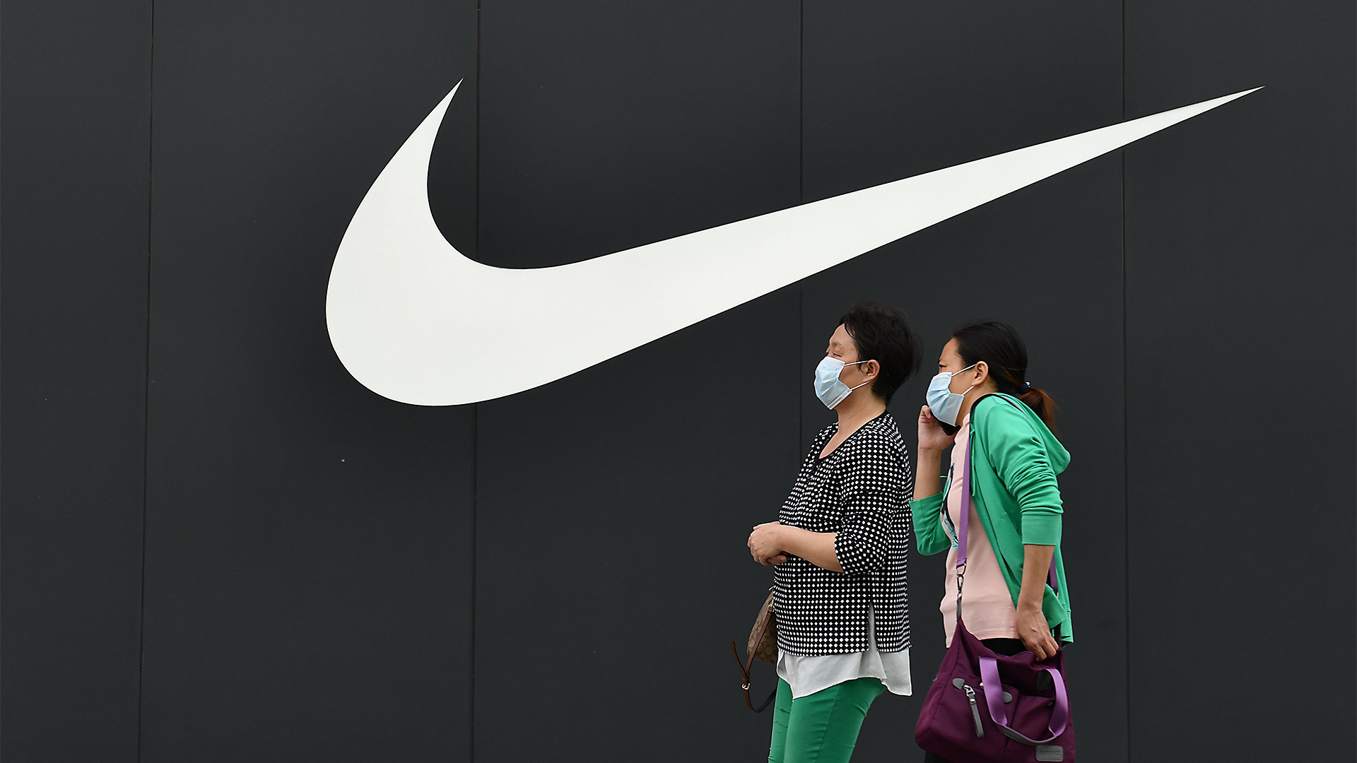 Zwei Chinesinnen gehen in Peking an einem Nike-Logo an einer Wand vorbei | picture alliance / An Xin / Cost