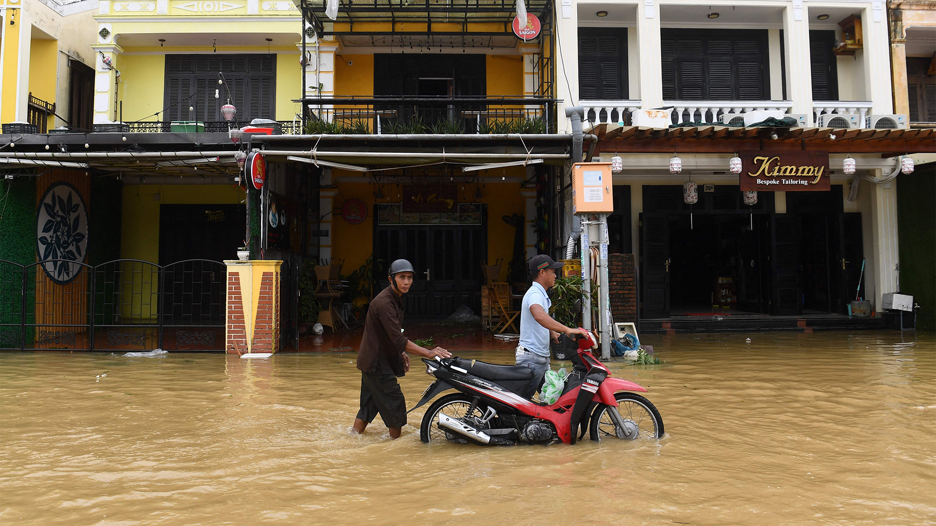 Zwei Männer schieben ein Motorrad durch eine überflutete Straße in der vietnamesischen Stadt Hoi An. | AFP