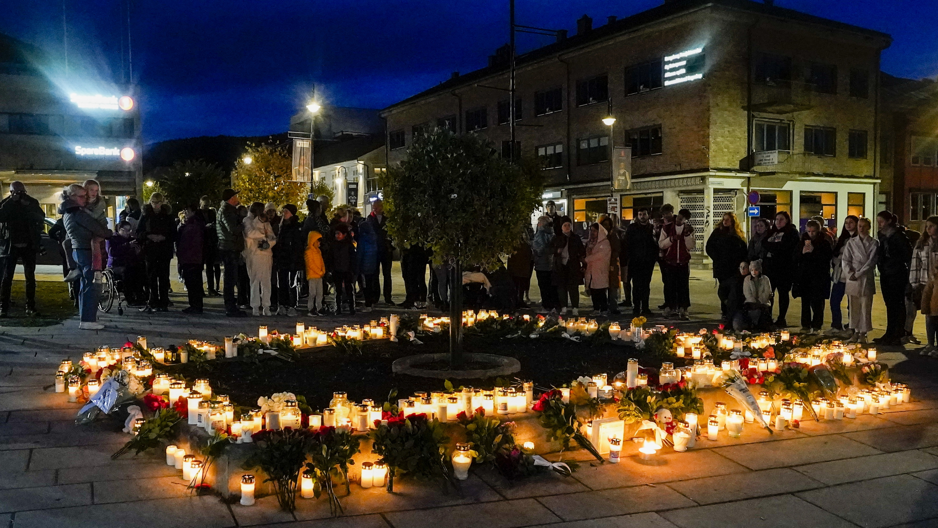 Personen stehen vor Blumen und Kerzen, die in Gedenken an die Opfer niedergelegt wurden. Nach der Gewalttat mit fünf Toten in der norwegischen Kleinstadt Kongsberg kann die Polizei einen terroristischen Hintergrund nicht ausschließen. | dpa
