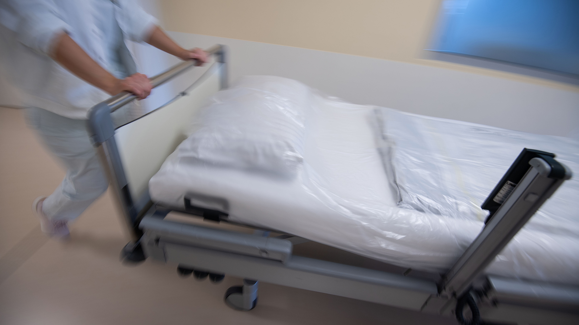 Eine Krankenpflegerin schiebt ein Krankenbett durch einen Gang einer Station | dpa