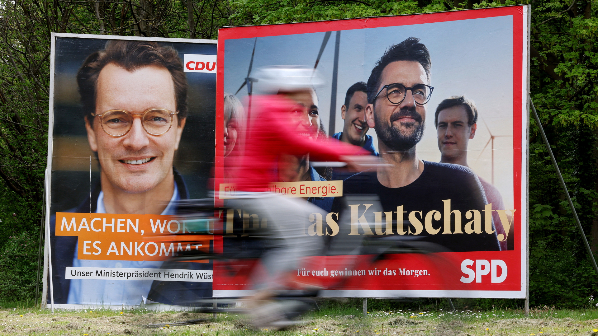 Wahlplakate mit Porträts der nordrhein-westfälischen Spitzenkandidaten von CDU, Ministerpräsident Hendrik Wüst (l), und SPD, Thomas Kutschaty (r), stehen auf einer Wiese. 