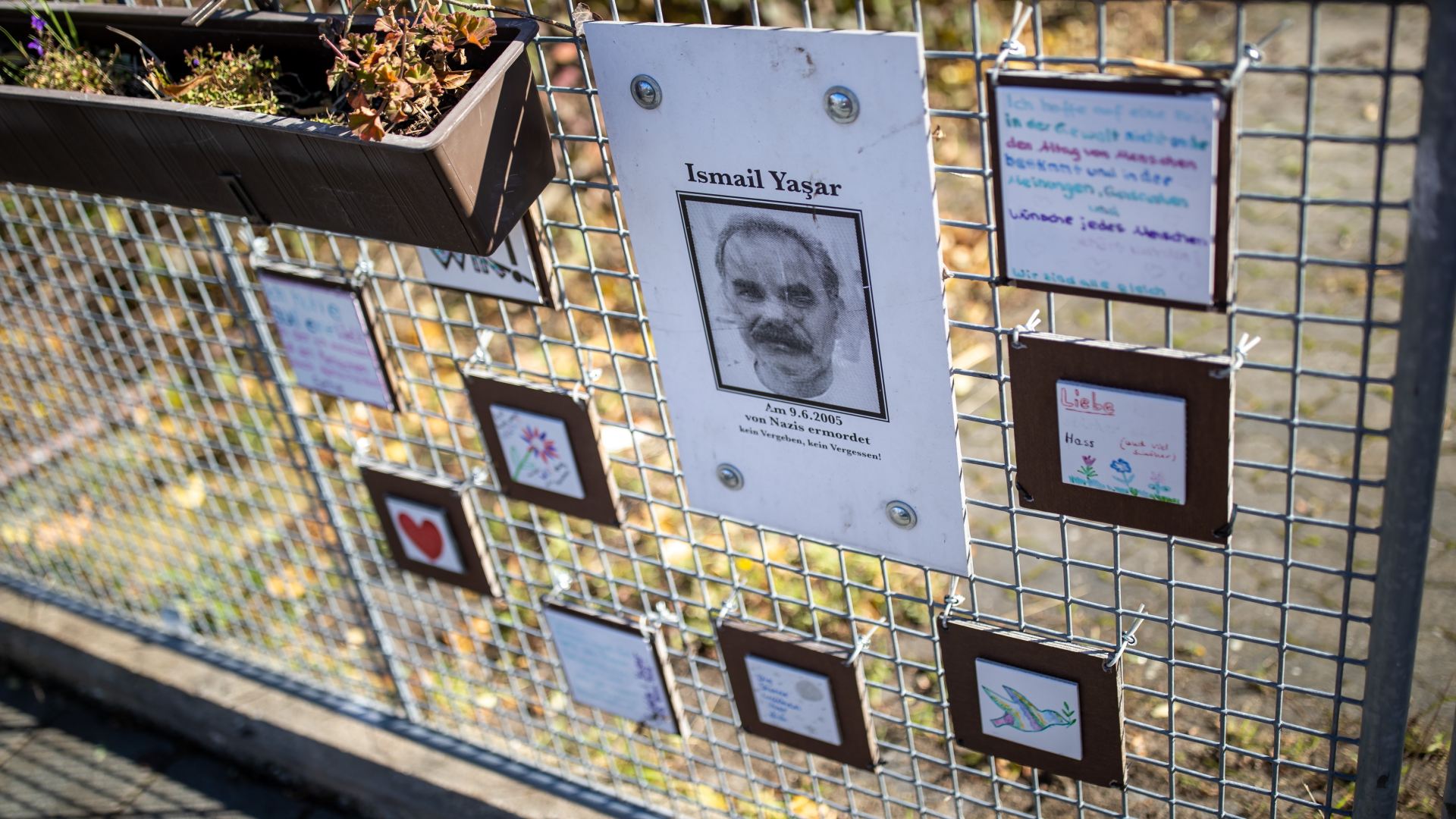 Eine Holztafel mit dem Abbild des vom NSU ermordeten Ismail Yasar hängt am Tatort an einem Zaun in Nürnberg. | dpa