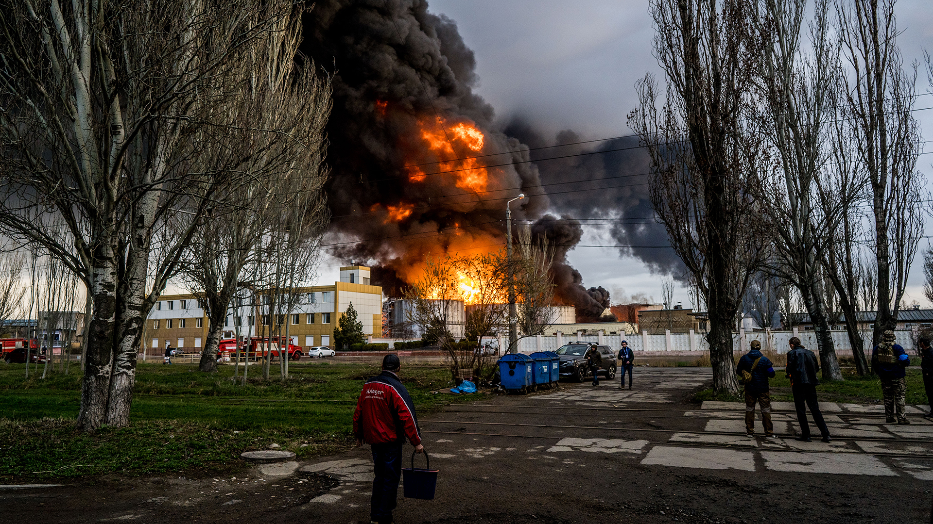 Personen stehen in Odessa (Ukraine) auf einer Straße und beobachten wie am Horizont Feuer und schwarzer Rauch aufsteigt. | dpa