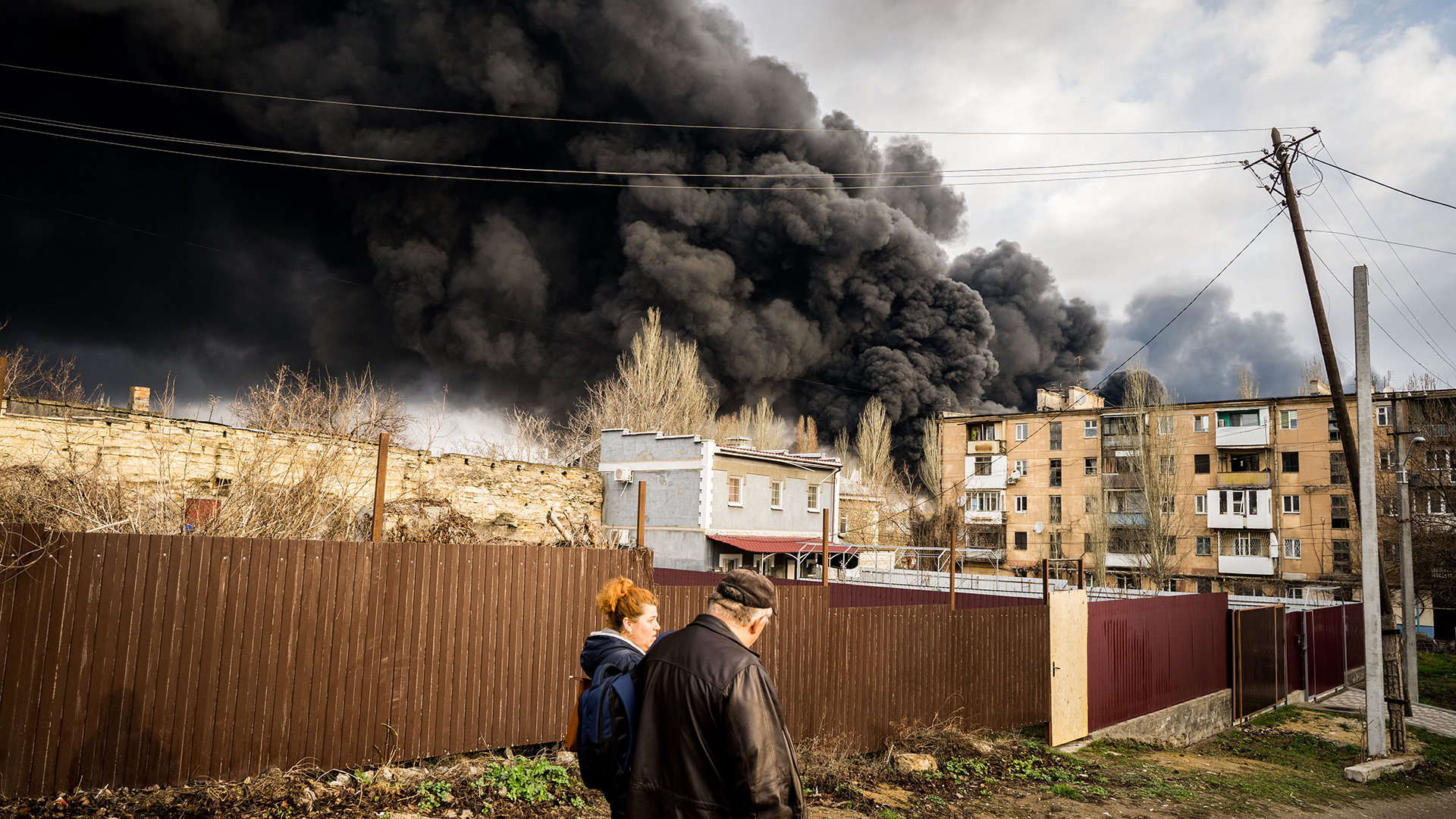 Zwei Personen gehen in Odessa (Ukraine) einen Weg entlang, während am Horizont schwarzer Rauch aufsteigt. | dpa