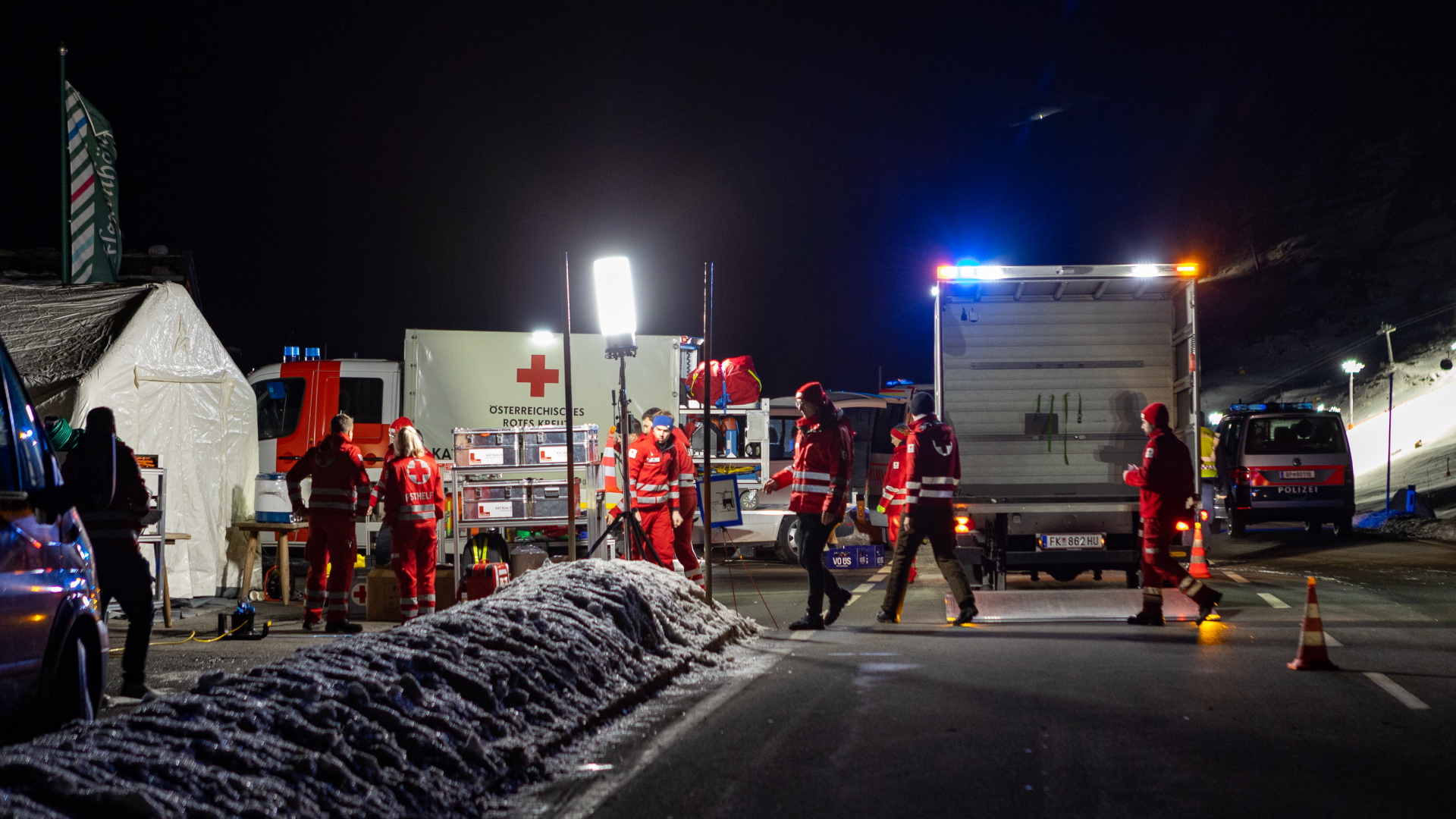 Im österreichsichen Arlberg stehen nachts Rettungskräfte rund um ihre Einsatzfahrzeuge. | dpa