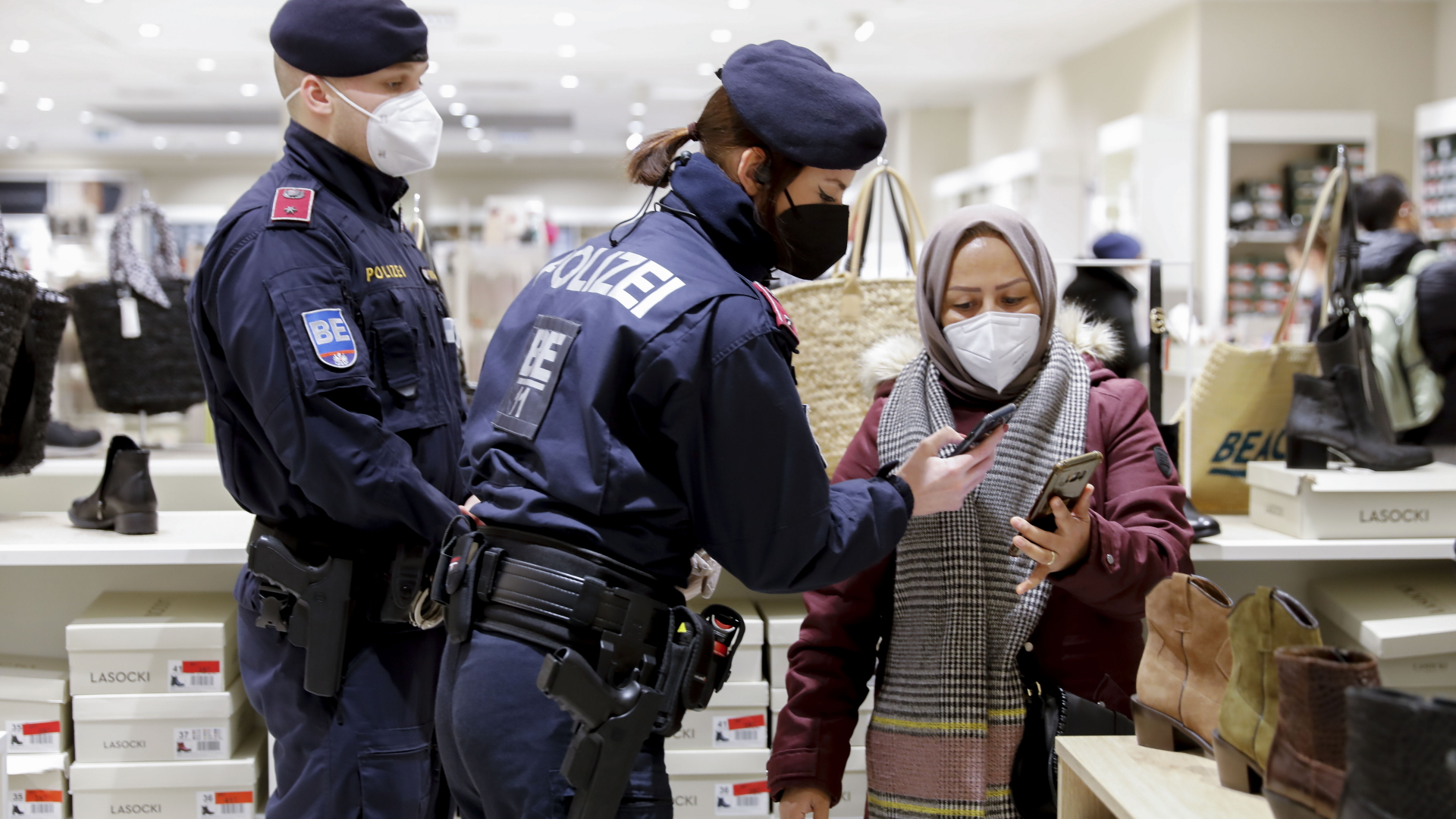 Zwei Polizeikräfte kontrollieren in einem Geschäft in Wien den Corona-Impfnachweis auf dem Handy einer Frau. | dpa