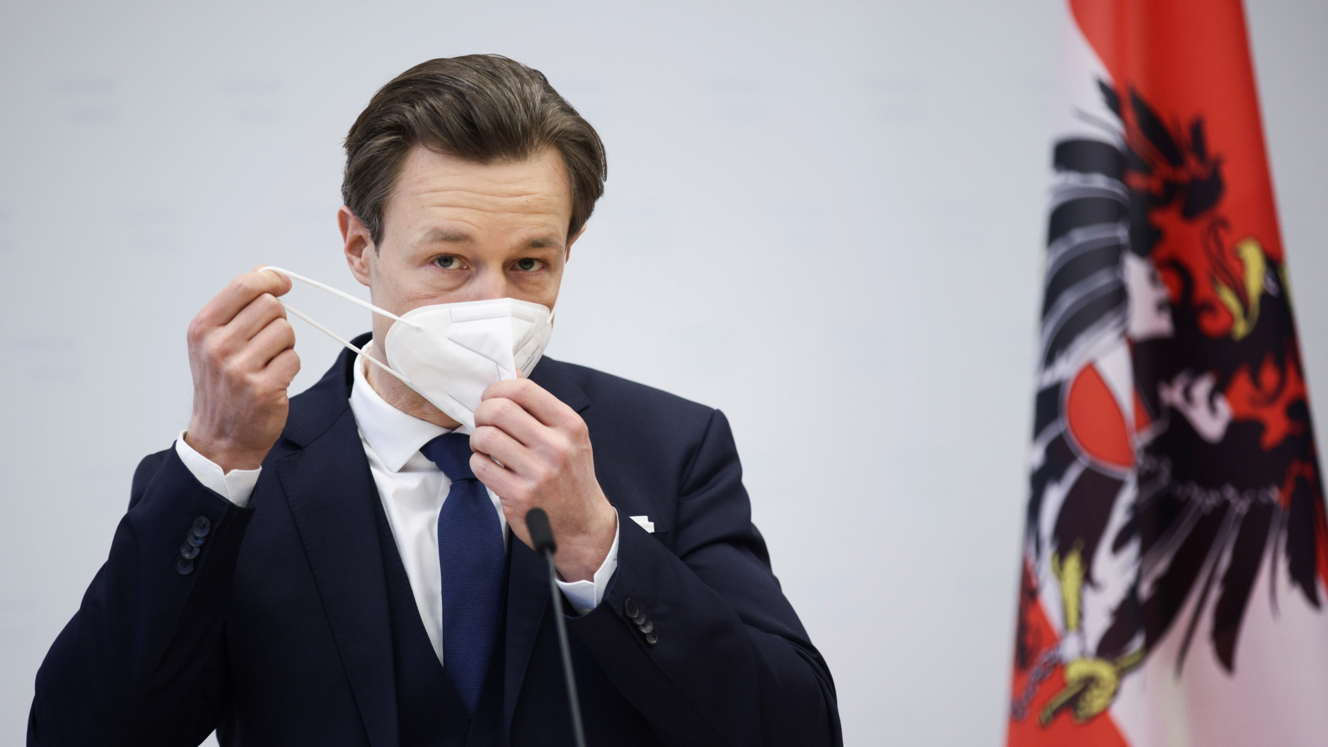 Der österreichische Finanzminister Blümel nimmt bei einer Pressekonferenz seine Schutzmaske ab.