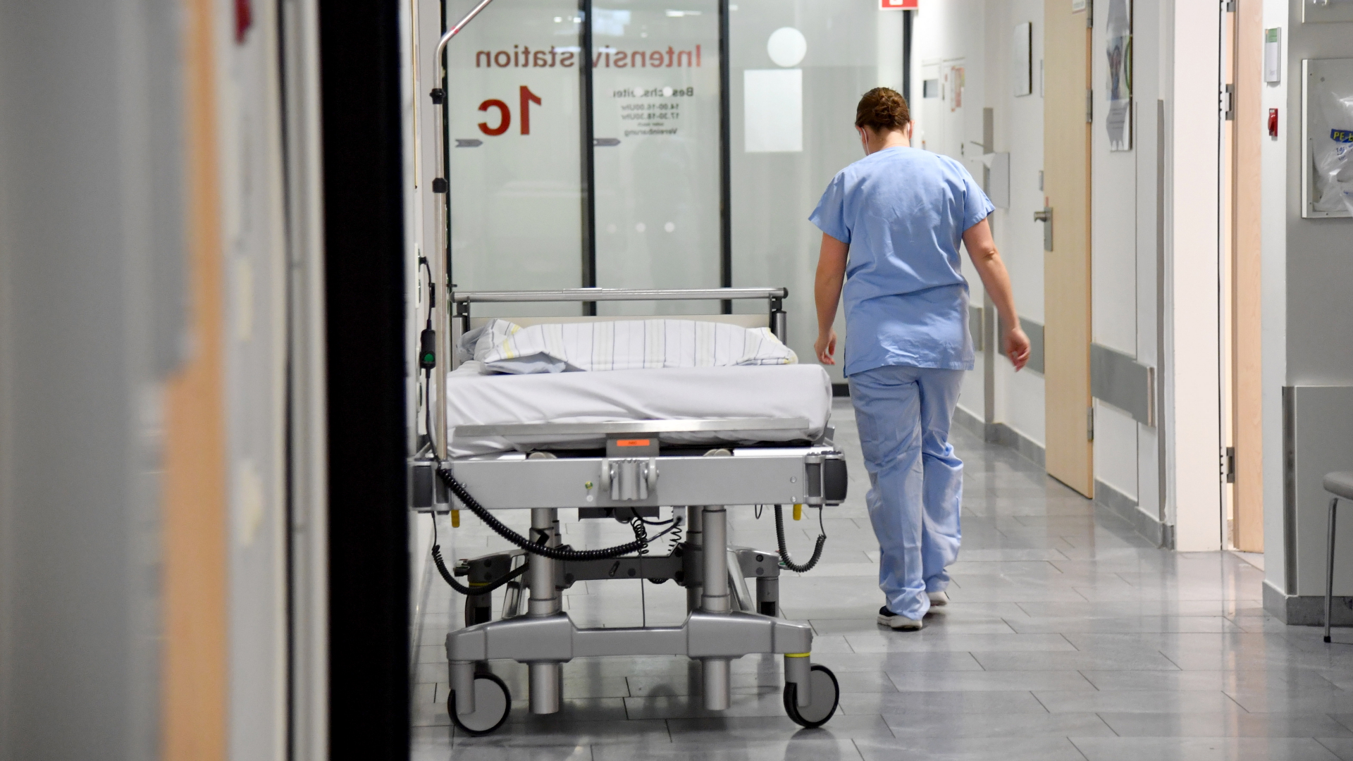 Ein Mitarbeiter im Gesundheitswesen geht auf der Intensivstation der Salzburger Landeskliniken den Flur entlang.  | dpa