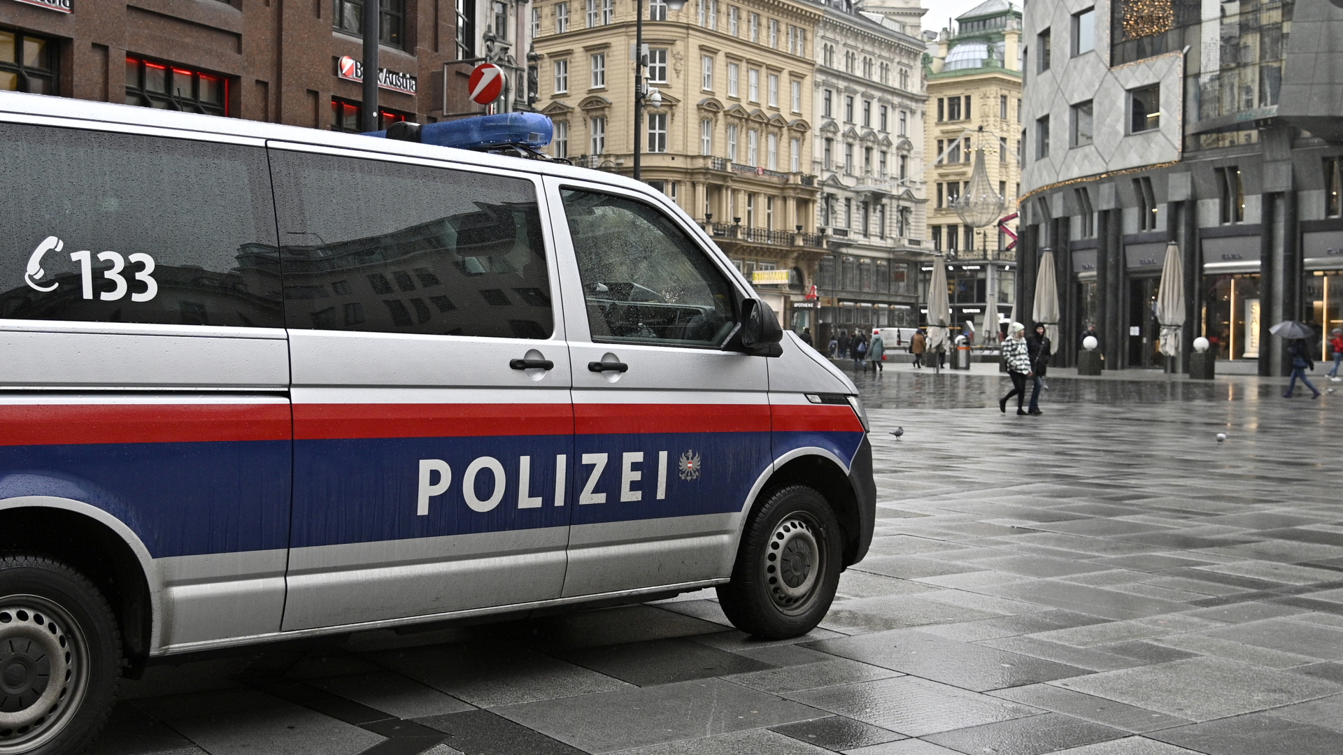 Ein Polizeiauto fährt durch eine Einkaufsstraße in Österreich (Archivbild). | dpa