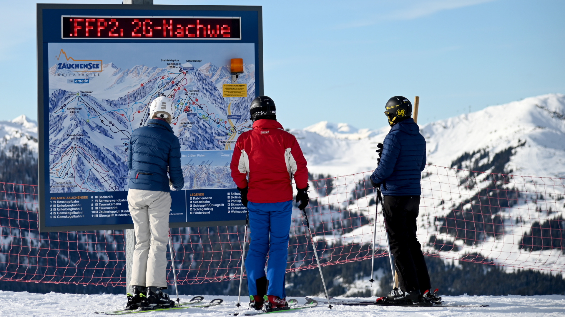 Skifahrer stehen vor einer Informationstafel mit der Aufforderung nach FFP2-Masken und 2G-Nachweis im österreichischen Skigebiet Altenmarkt-Zauchensee. | dpa