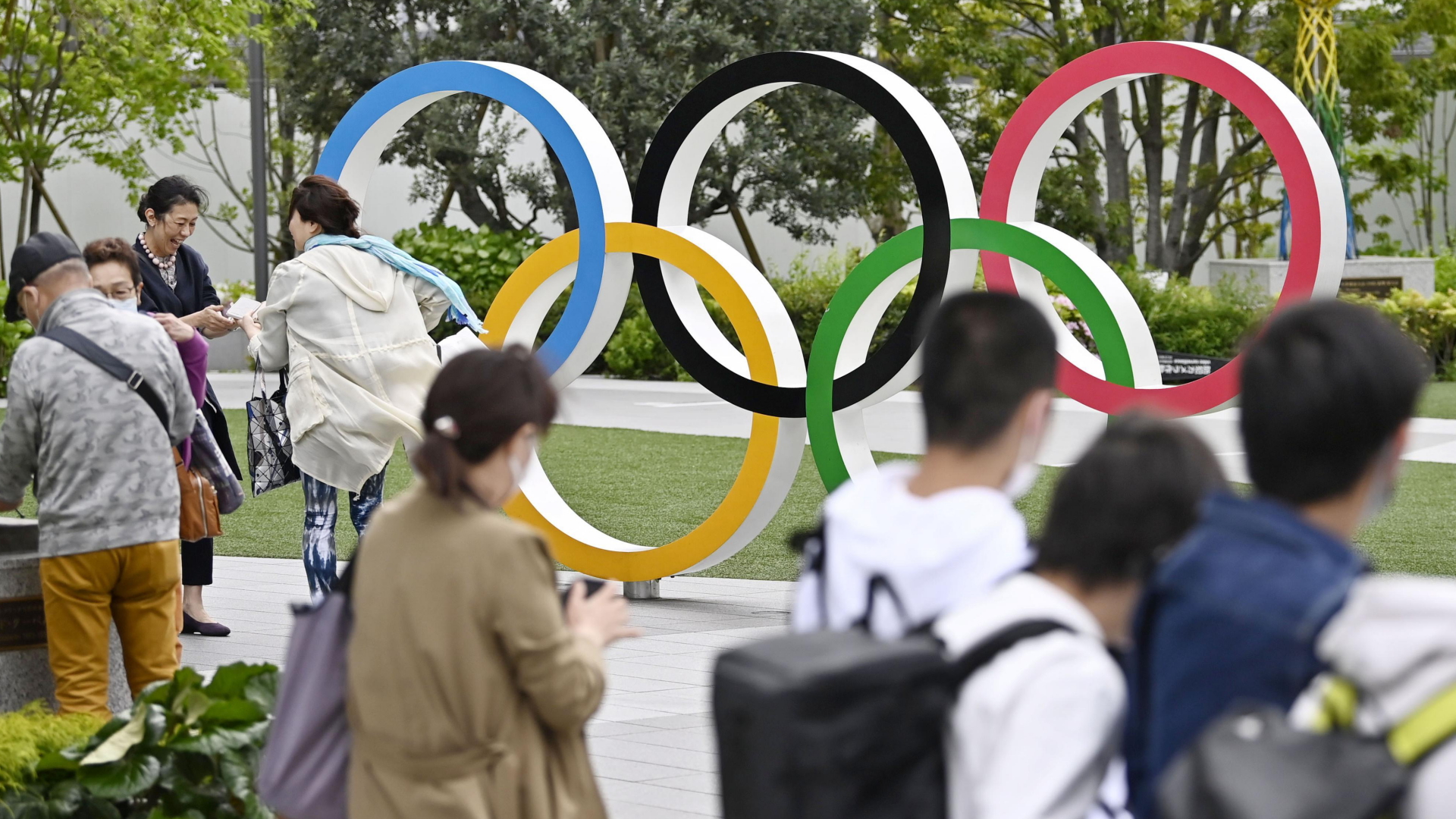  Einige Menschen stehen vor den Olympischen Ringen im Shinjuku-Bezirk von Tokio. | dpa
