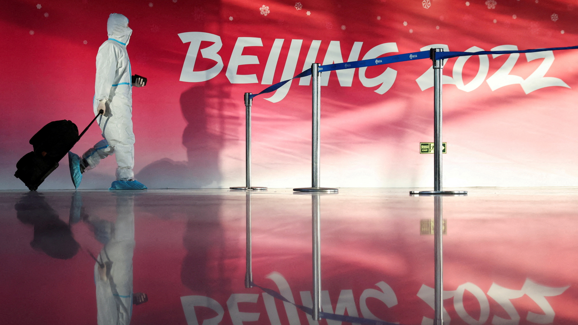 Eine Person im Sicherheitsanzug geht am Flughafen von Peking an dem Logo der Olympischen Winterspiele 2022 vorbei | REUTERS