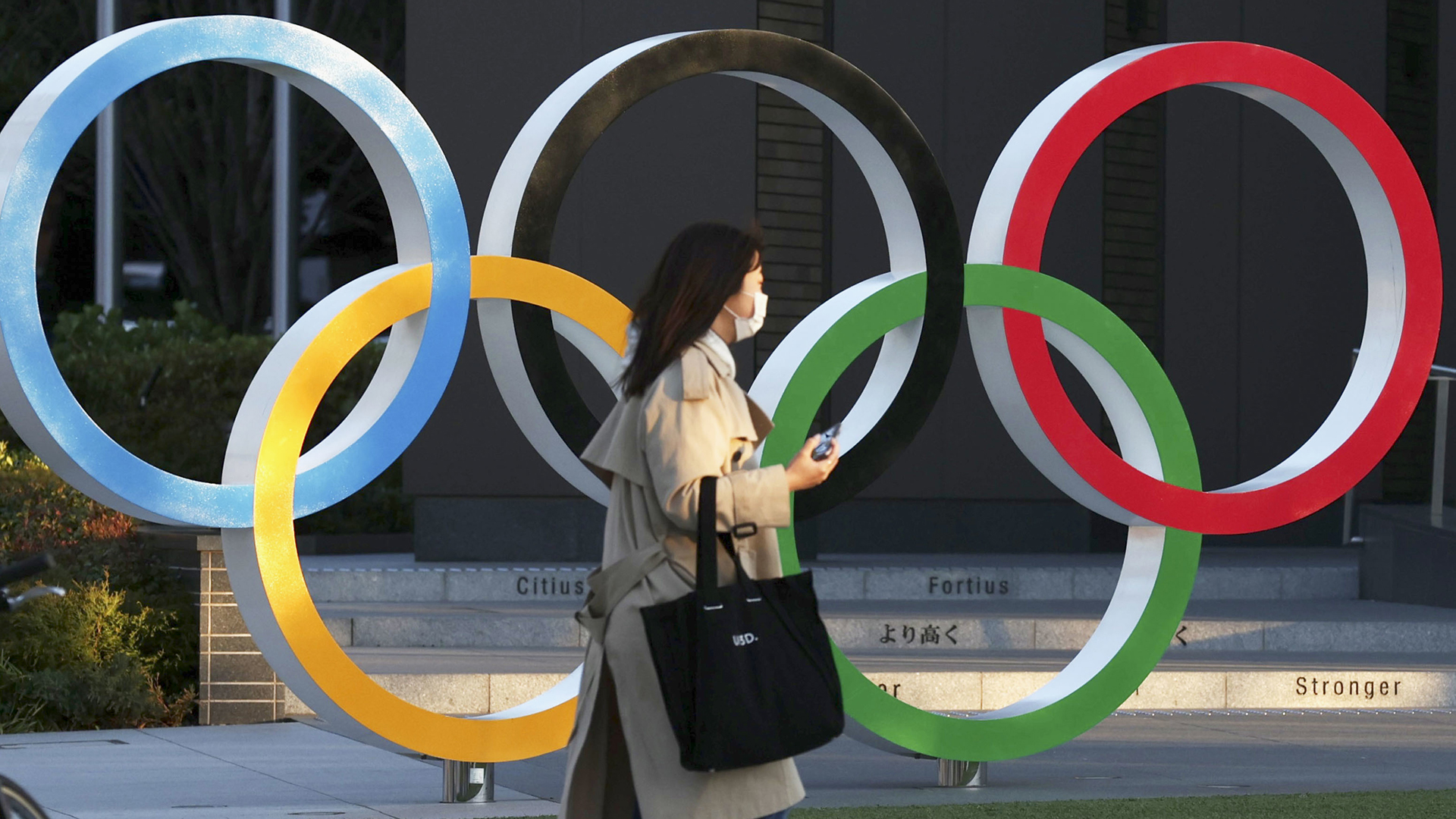 Eine Frau mit einer Mundschutzmaske geht an einer Skulptur der Olympischen Ringe an der Shinjuku-Station in Tokio vorbei. | dpa