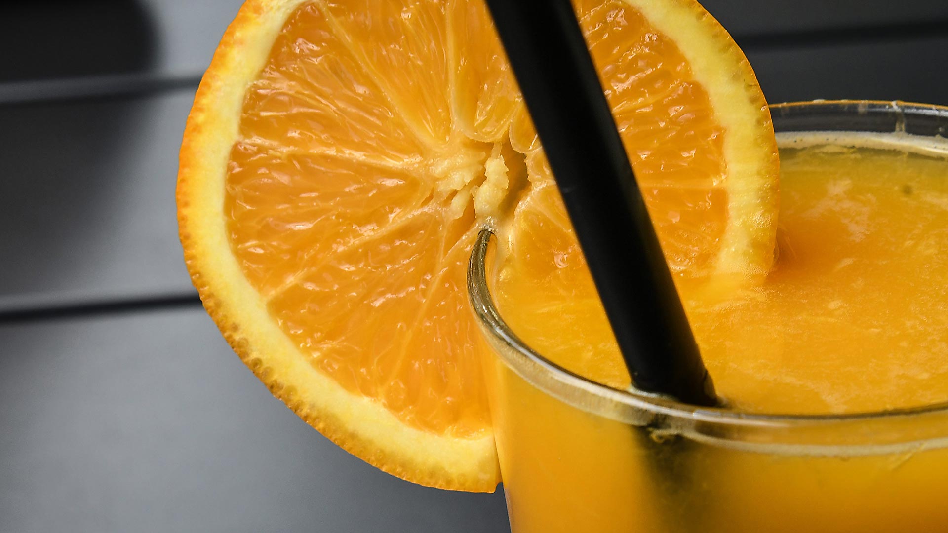 Nahaufnahme einer Orangenscheibe, die auf ein Glas mit Orangensaft gesteckt wurde.