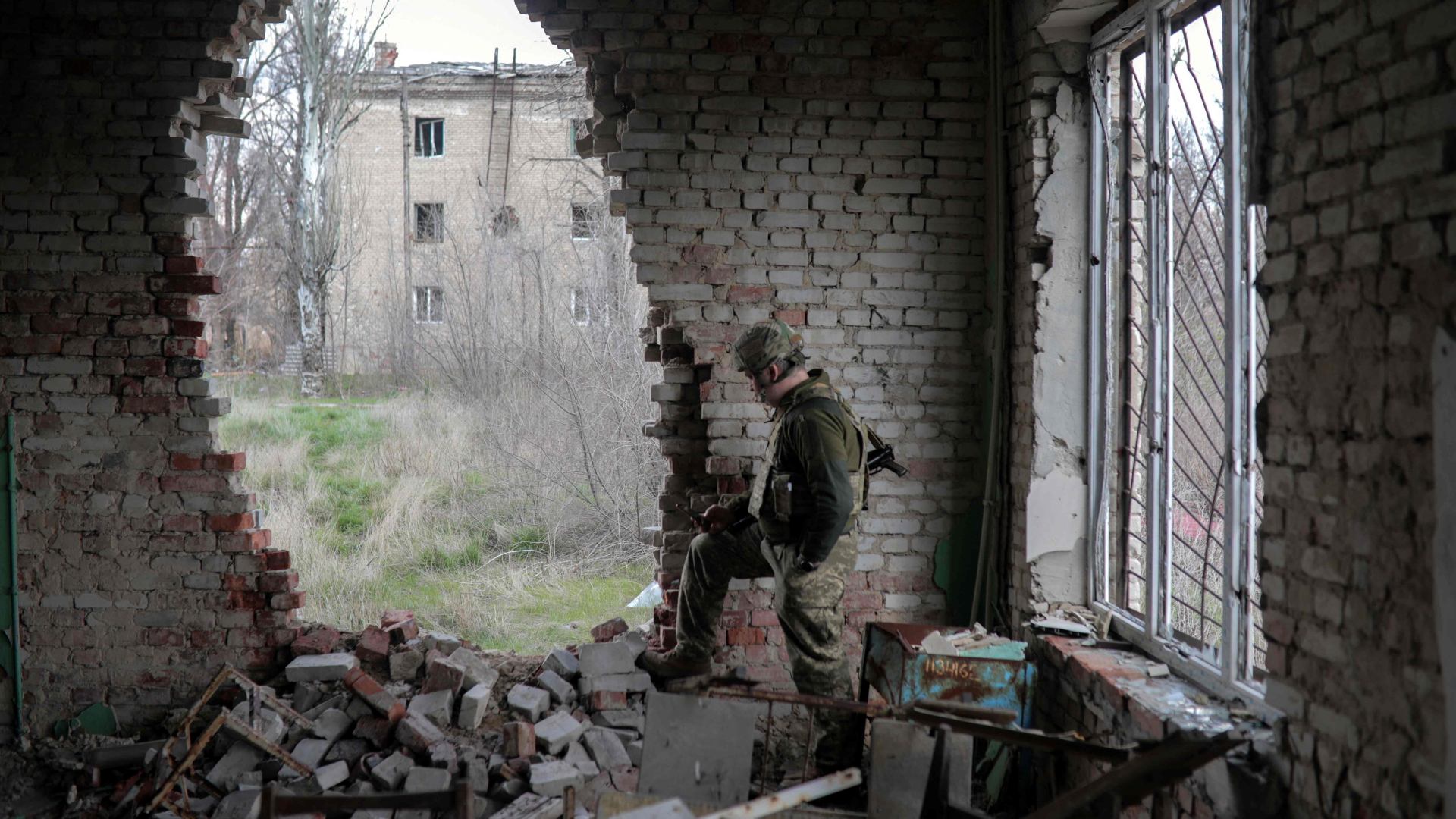 Ein Ukrainer in Kampfmontur steht an der Wand eines zerstörten Hauses in Pisky, nahe Donezk. | AFP