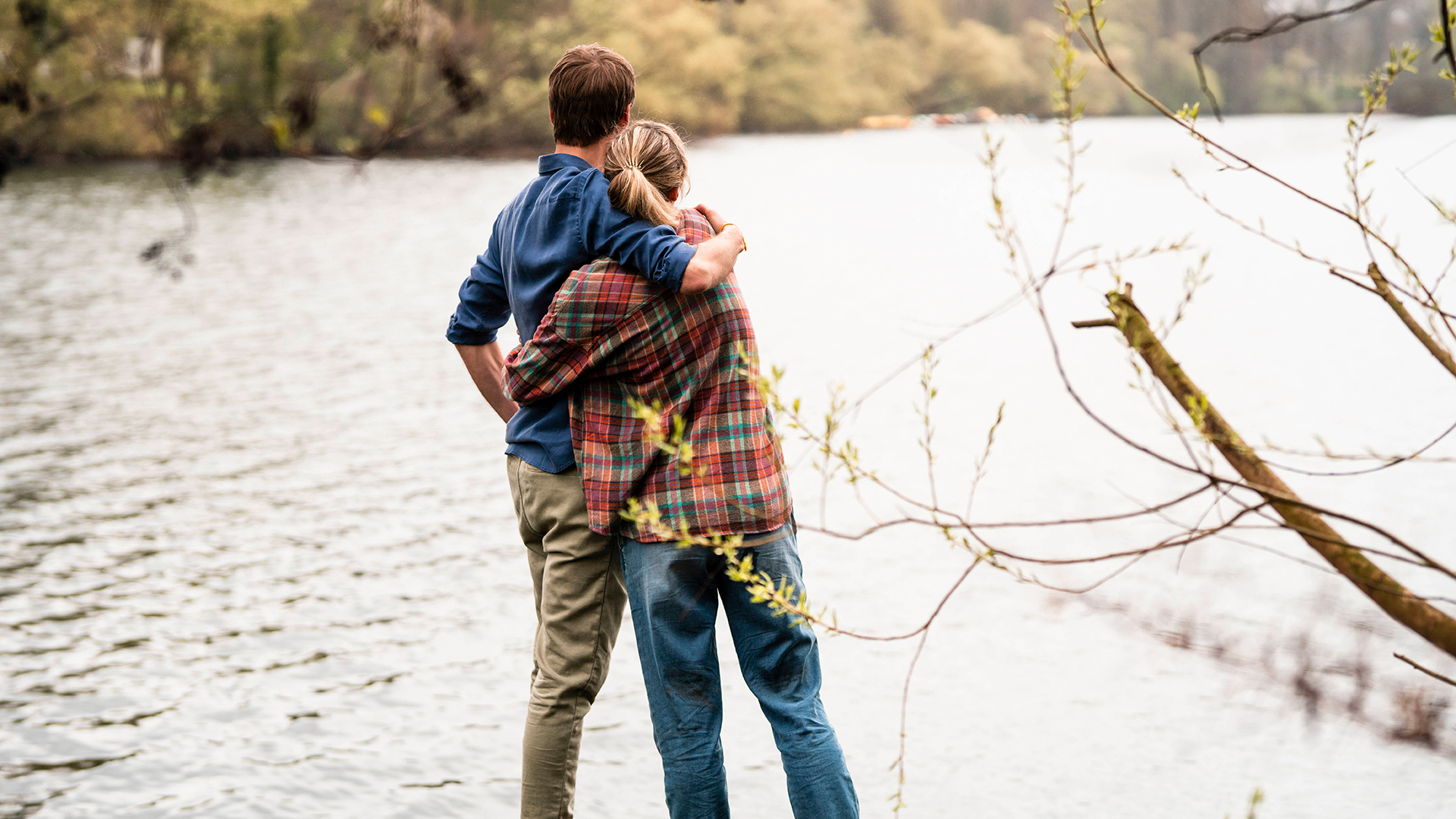 Ein Paar umarmt sich und guckt auf einen See. | IMAGO/Westend61